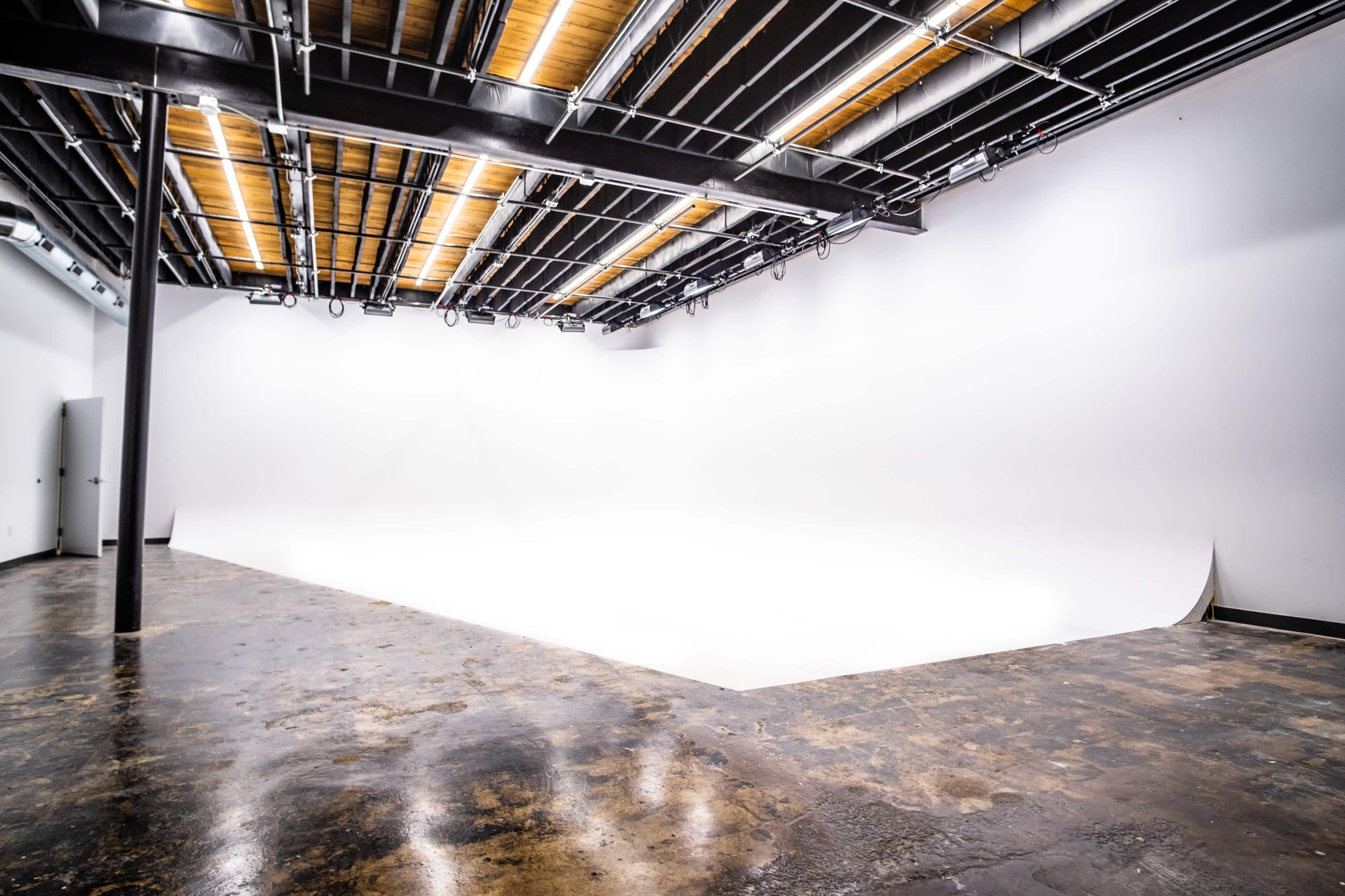 A spacious, empty photography studio with a seamless white backdrop and a polished concrete floor.