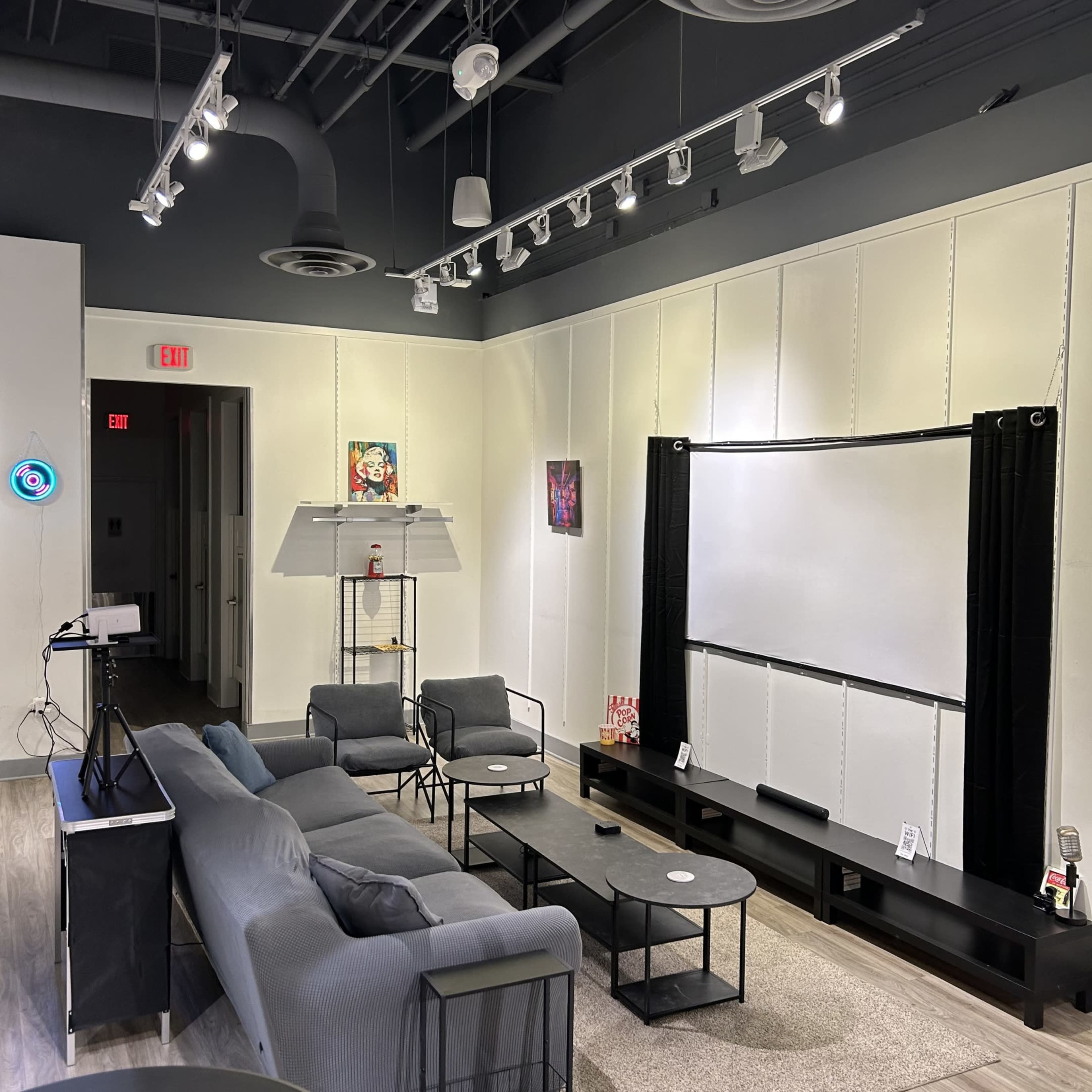 The image shows a modern, minimalist room with a projector screen, comfortable seating, and dim lighting fixtures.