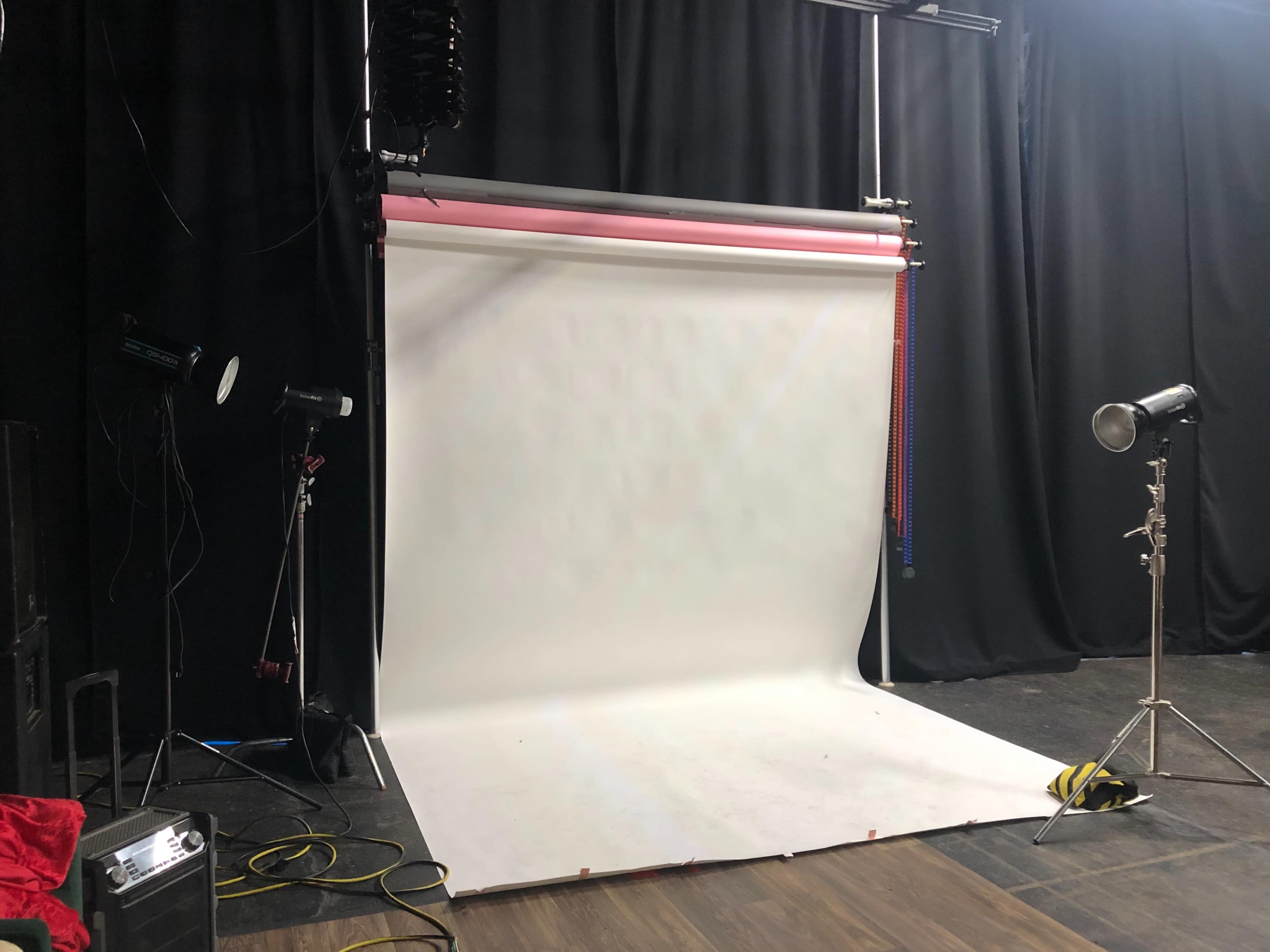 A photography studio setup with a white backdrop, lighting equipment, and dark black curtains.