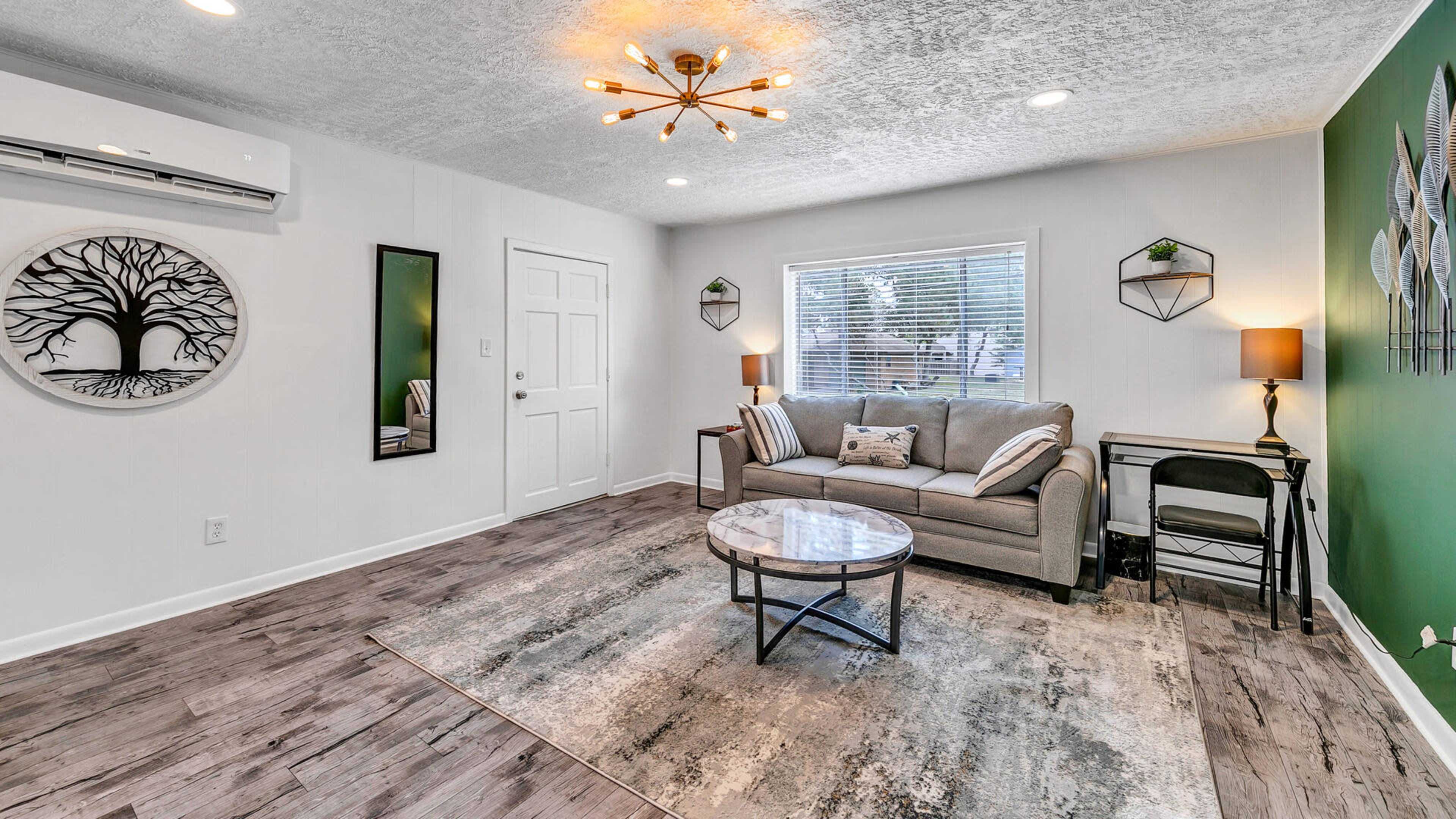 A modern living room with a gray sofa, a round coffee table, and decorative items on the walls and shelves, complemented by a green accent wall.
