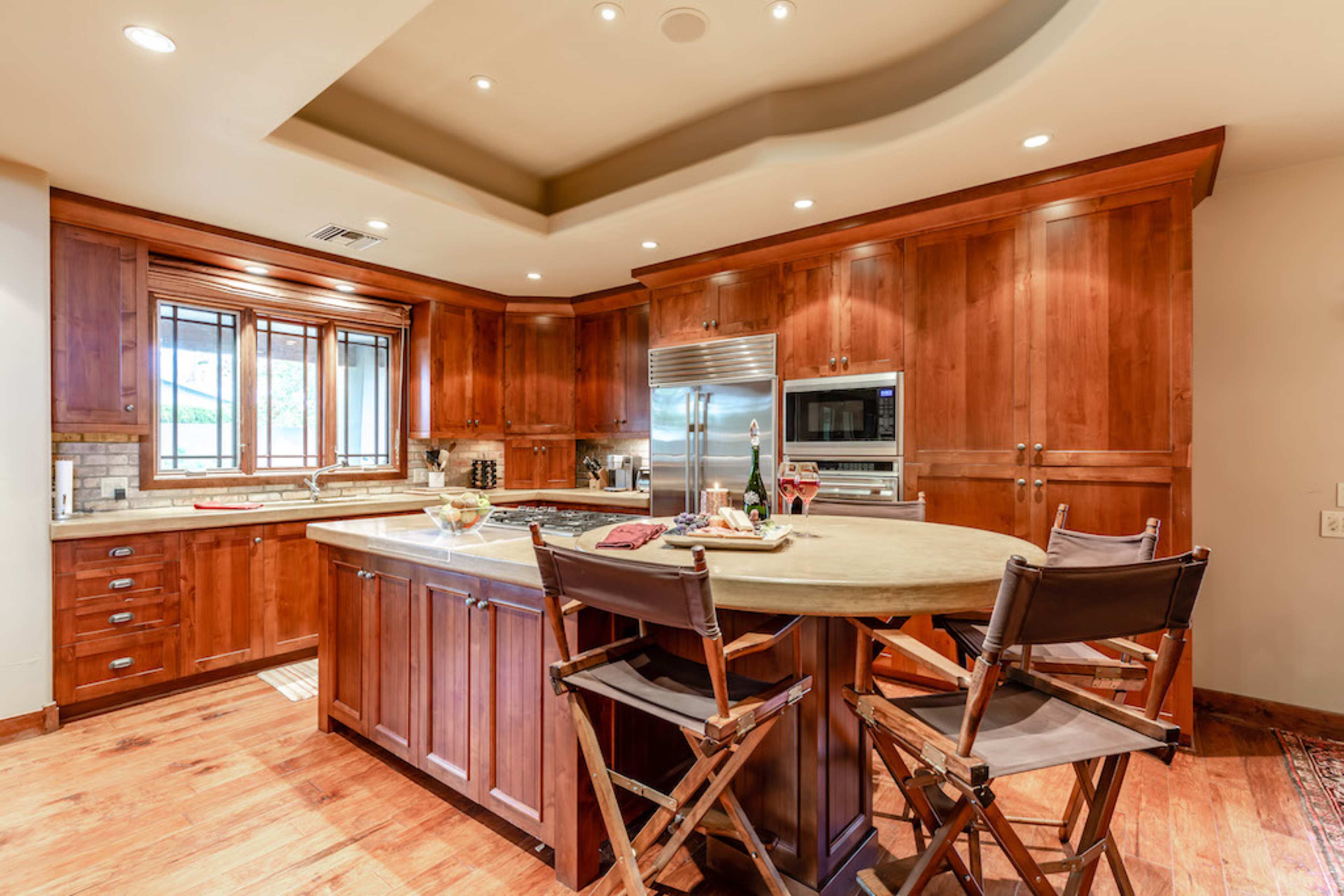 A modern kitchen with wooden cabinets, a large island with seating, and stainless steel appliances.