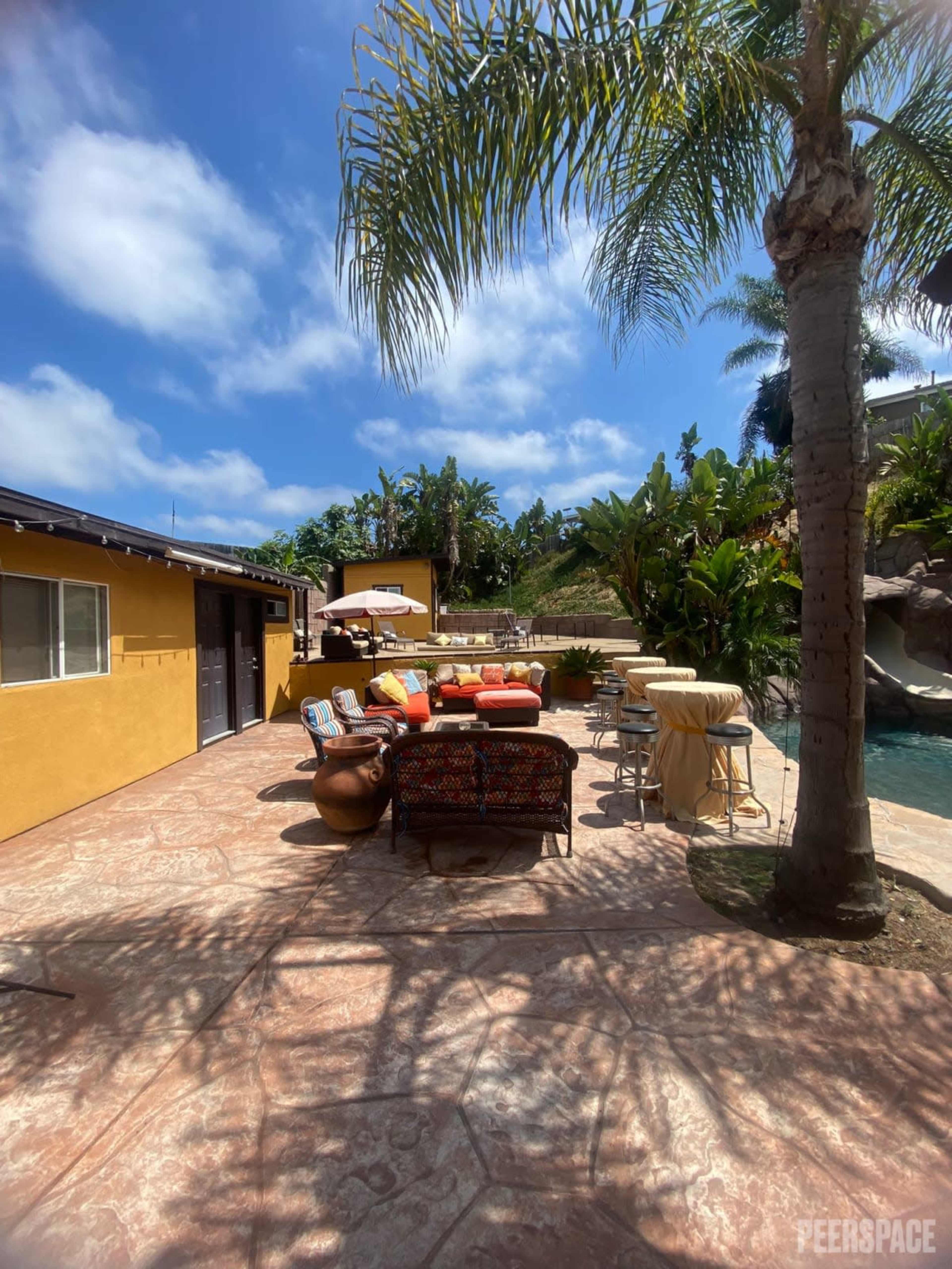 A patio area with colorful seating and a pool surrounded by tropical plants under a partly cloudy sky.