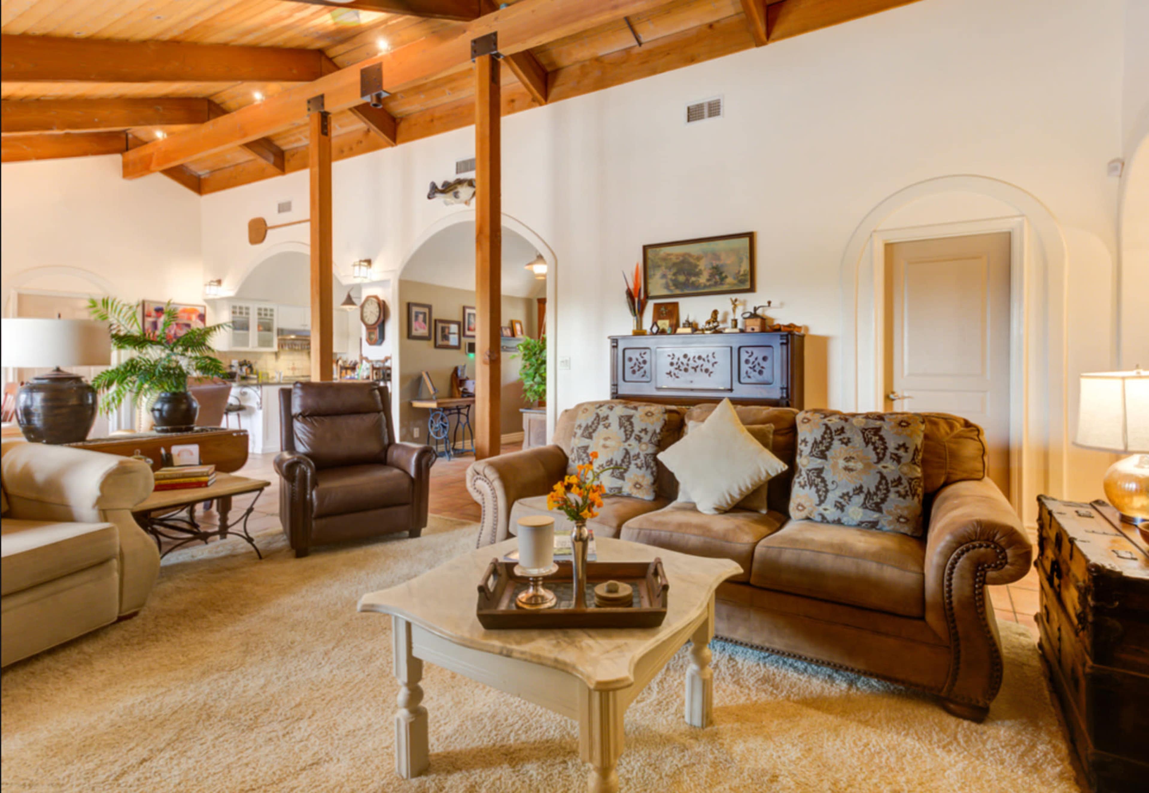 A cozy living room with a beige sofa, a wooden coffee table on a light carpet, and exposed wooden beams on the ceiling.
