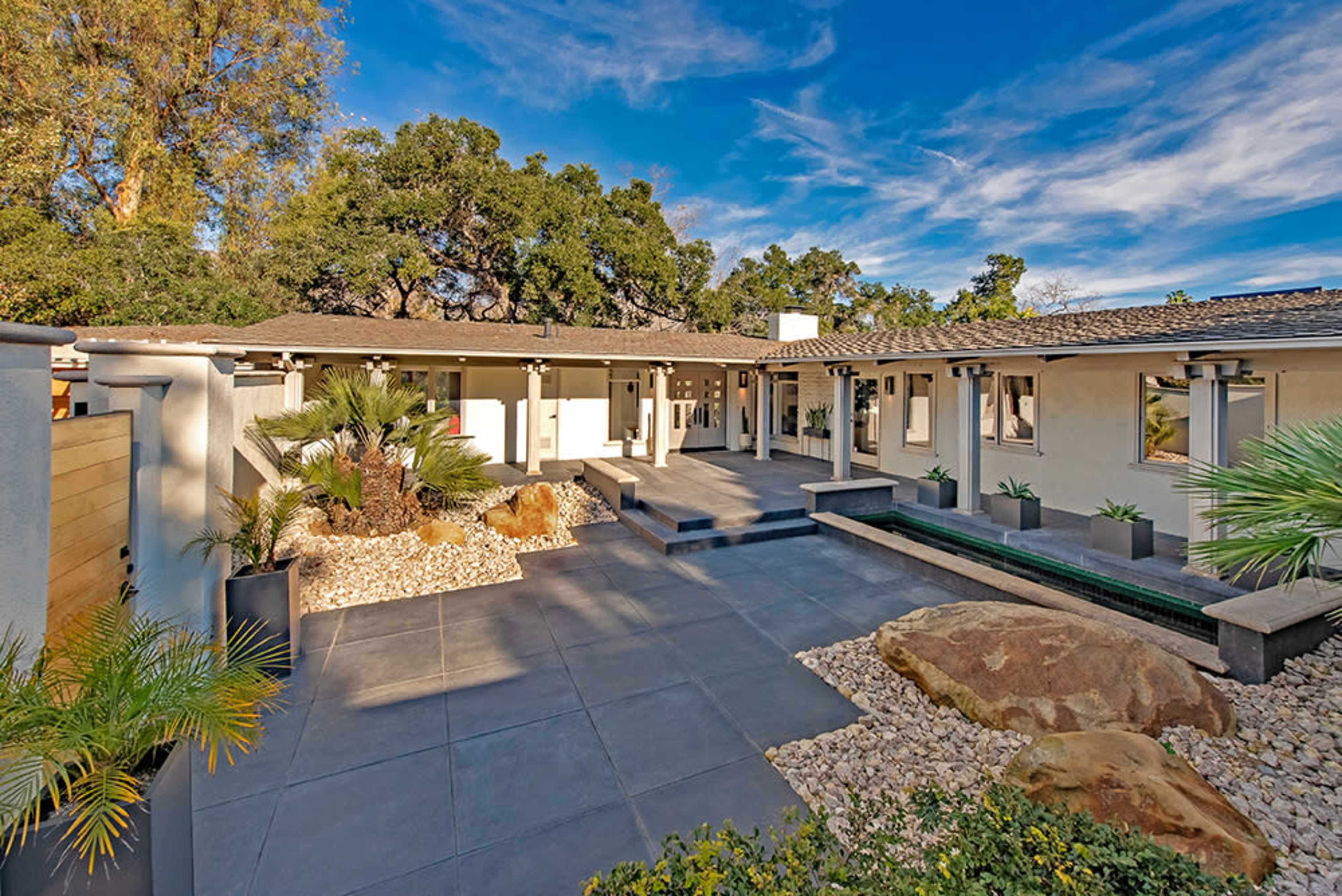 A modern courtyard features a combination of stone pathways, landscaped plants, and a central rock display surrounded by a single-story building.