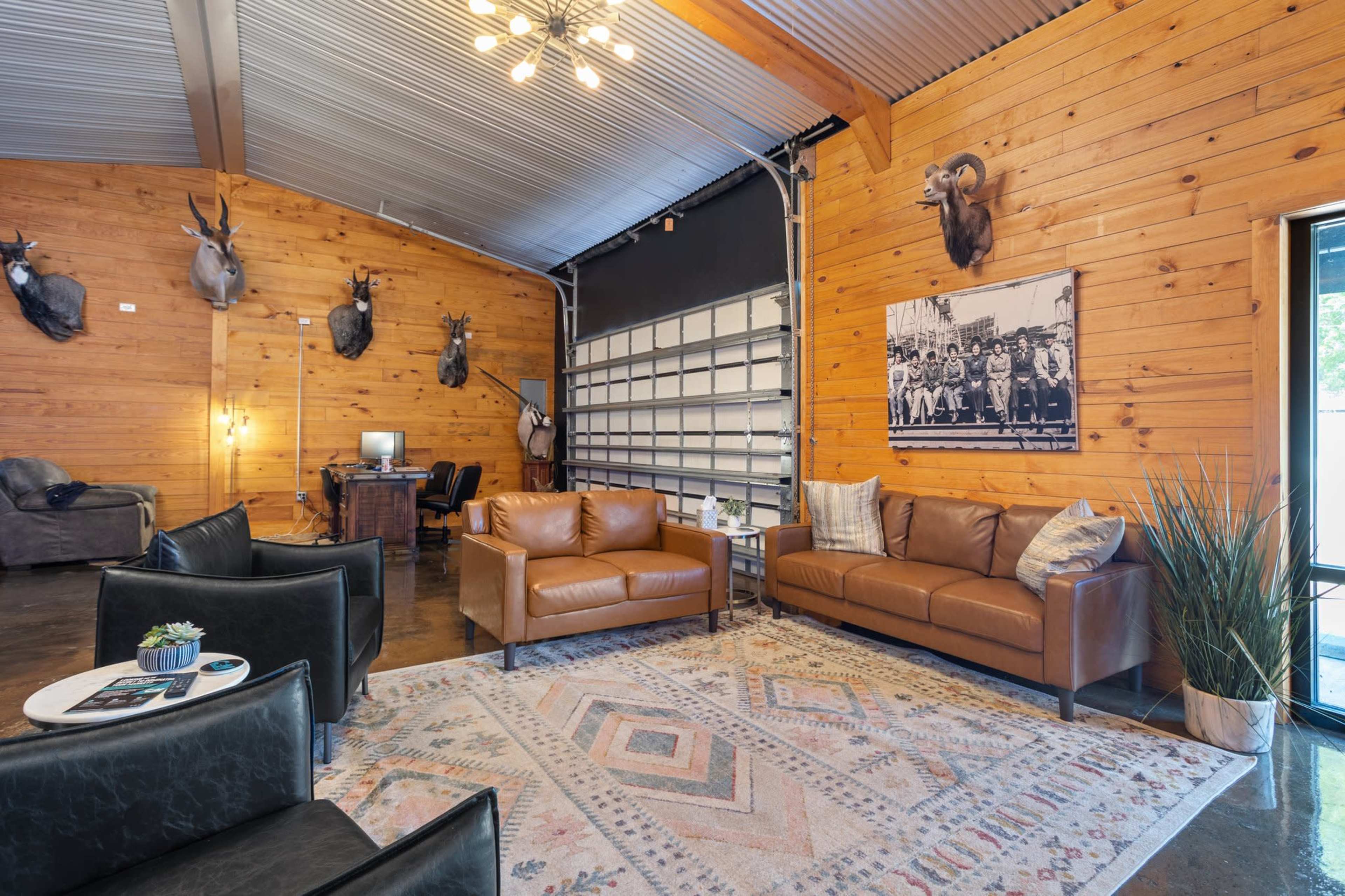 A spacious lounge with wooden walls, featuring mounted animal heads, leather sofas, a large rug, and a desk area.