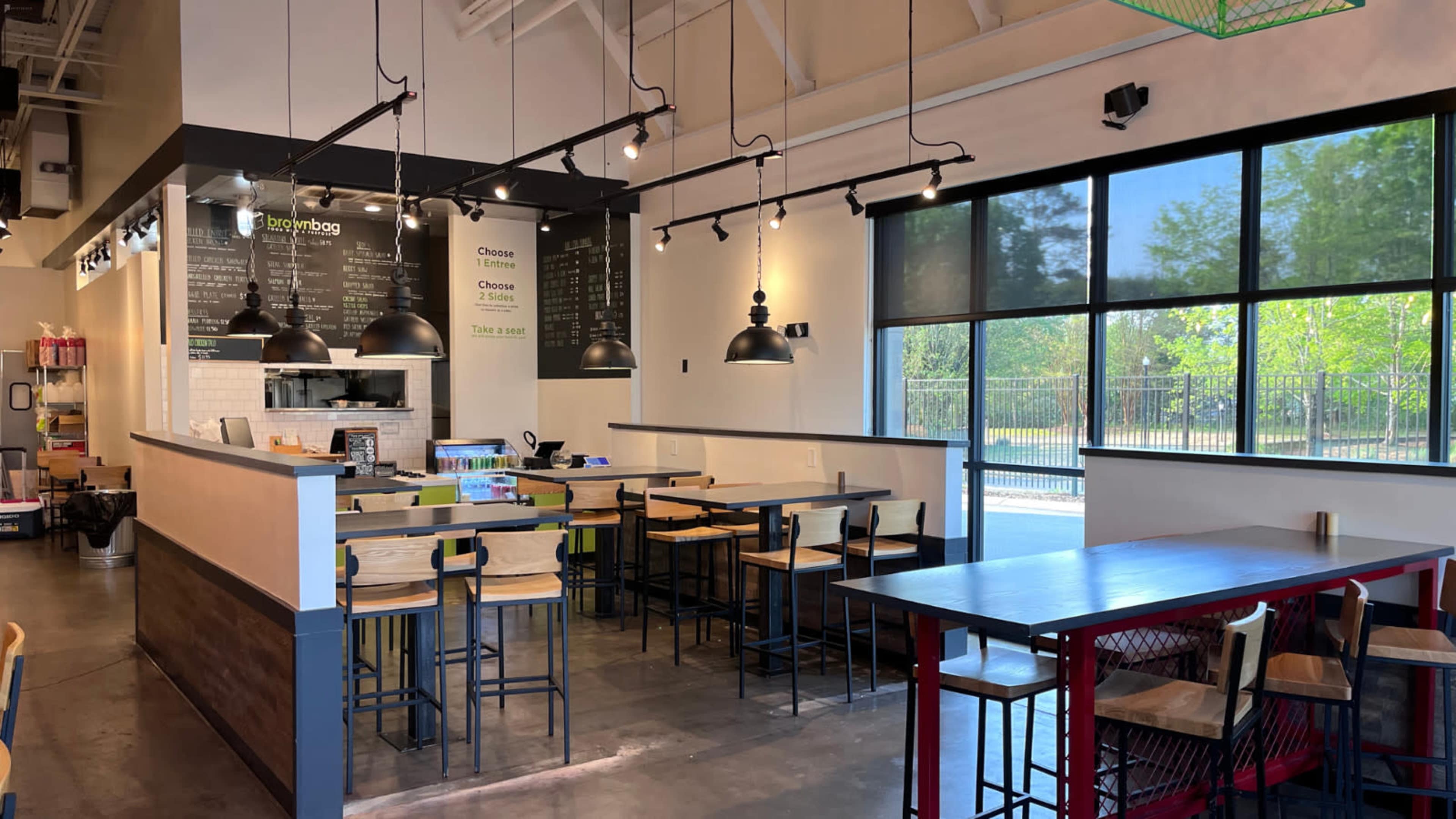 A modern café interior with wooden seating, overhead lights, a counter displaying the menu, and large windows allowing natural light to enter.