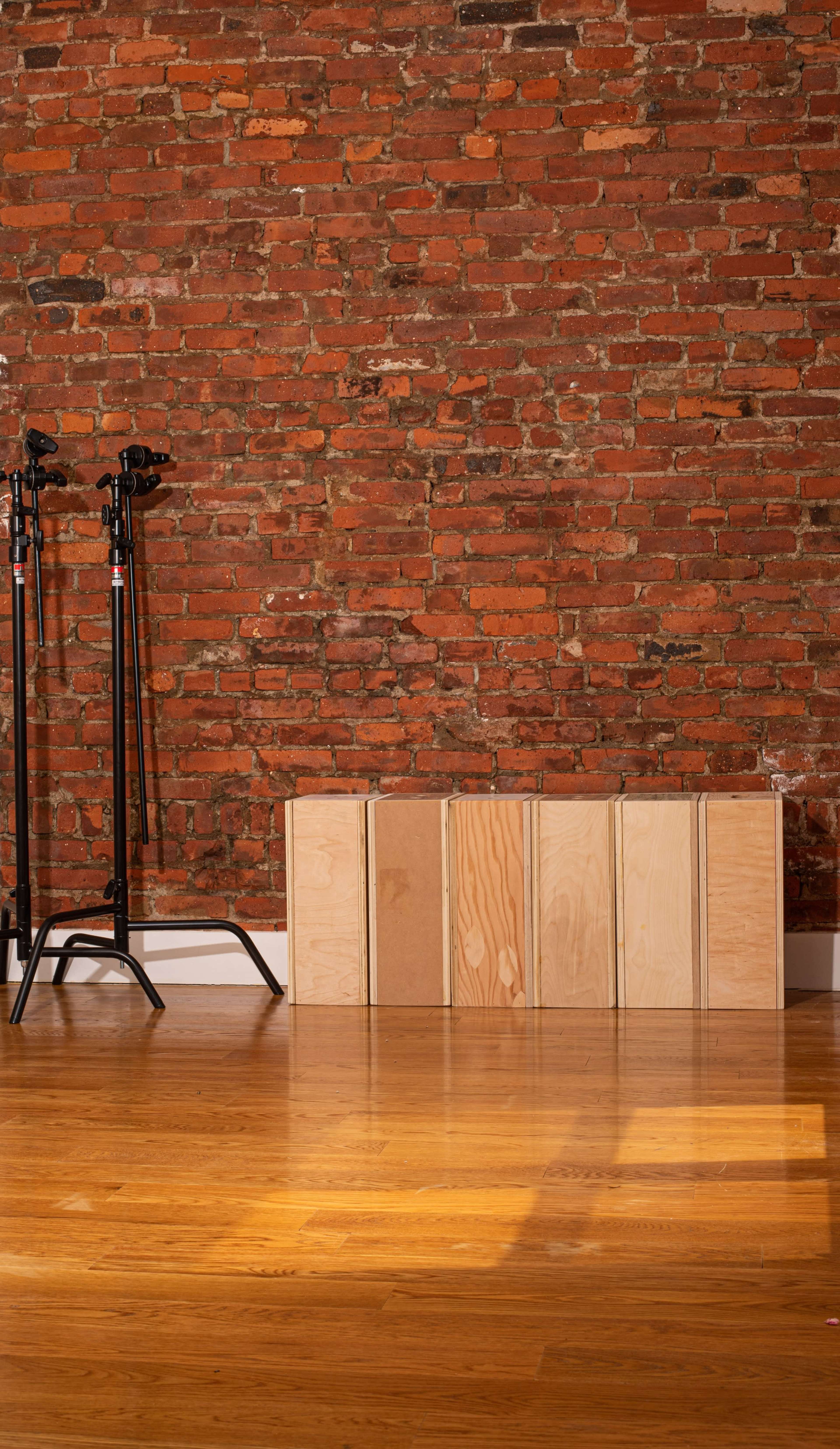 A wooden box placed on a hardwood floor in front of a brick wall, with two light stands positioned on the left side.
