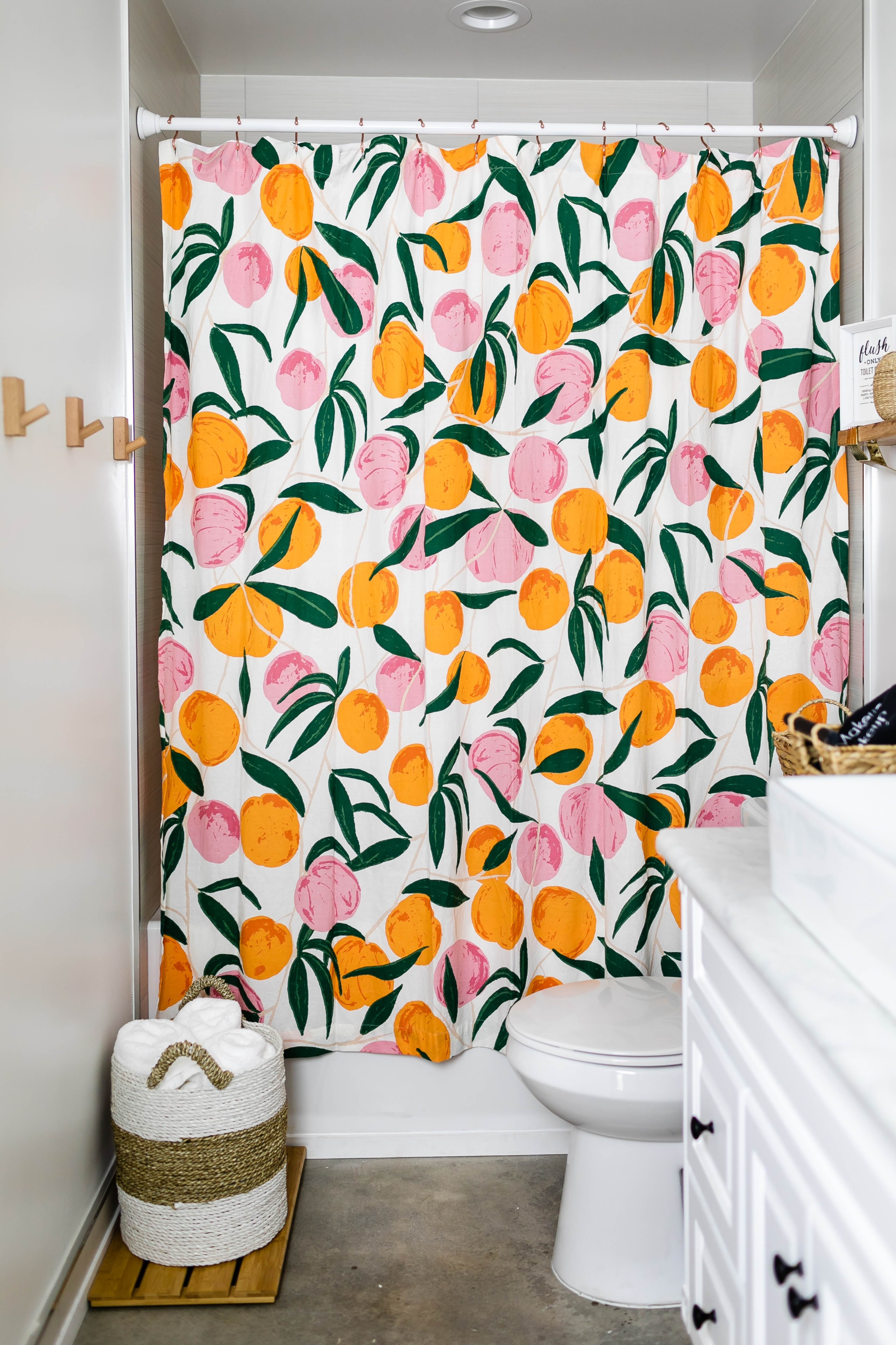 A bathroom with a colorful shower curtain featuring a fruit pattern, a white toilet, and a wooden stool.