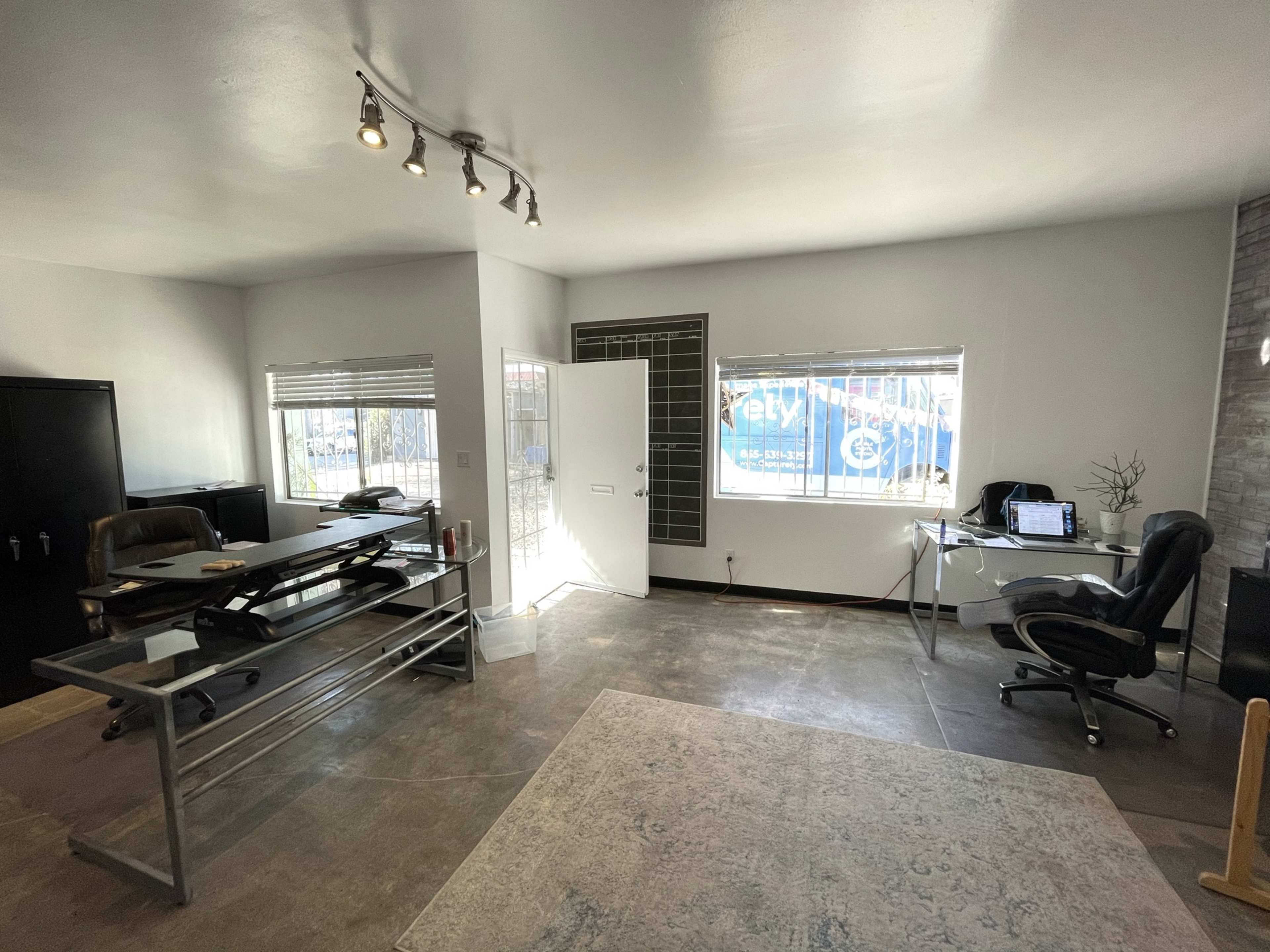 The image shows a modern office space with a desk, chair, and large windows allowing natural light in.