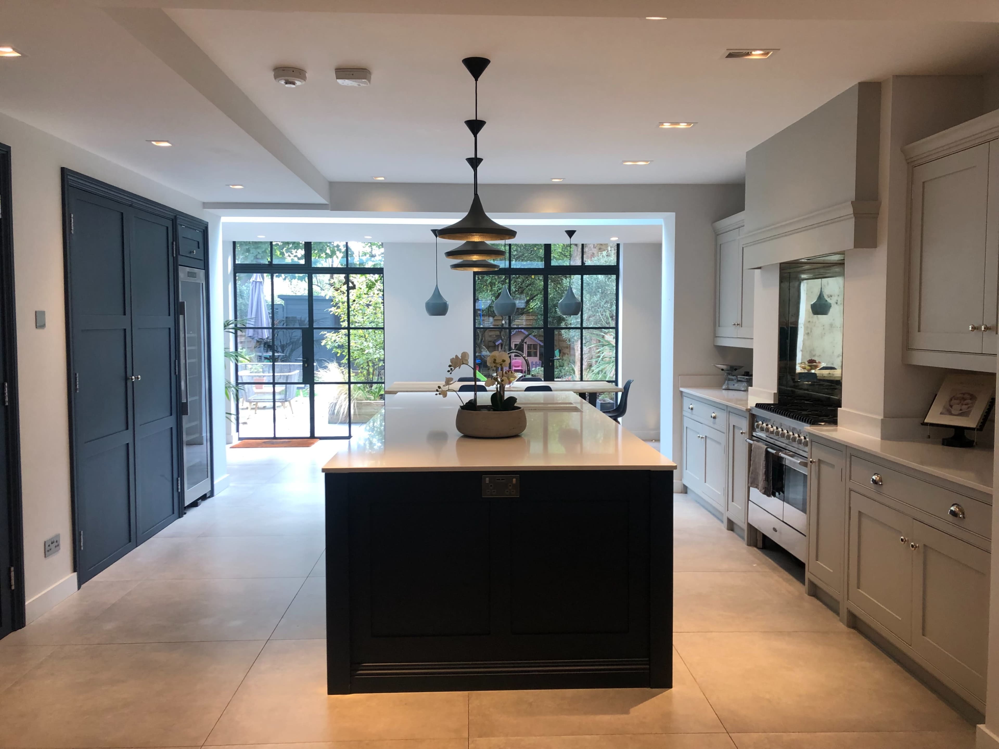 The image shows a modern kitchen with a central island, sleek cabinetry, and large windows overlooking a garden.
