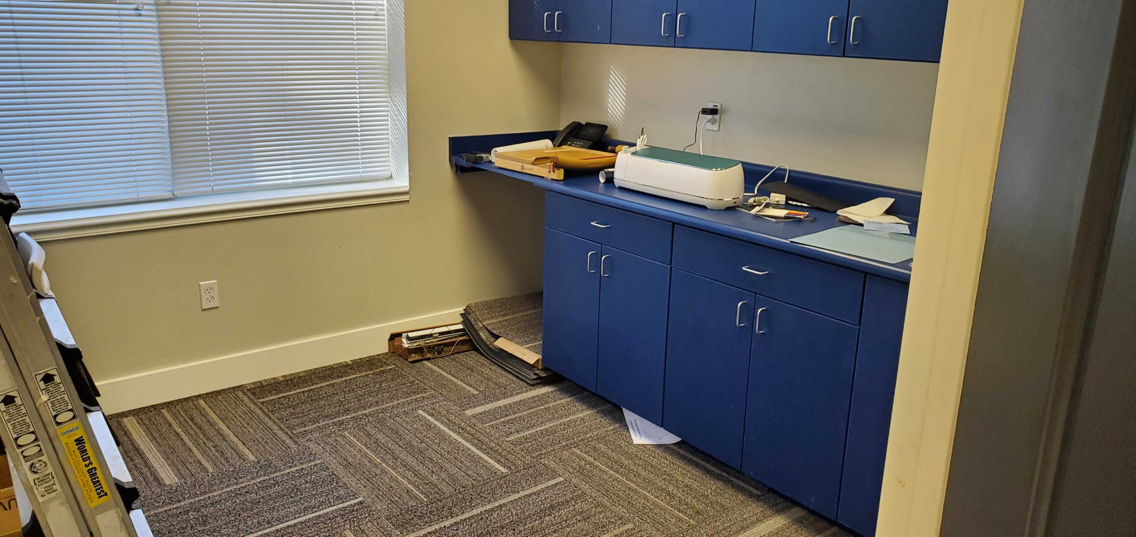 A small office space with a blue countertop, cabinets, and scattered items on the floor.