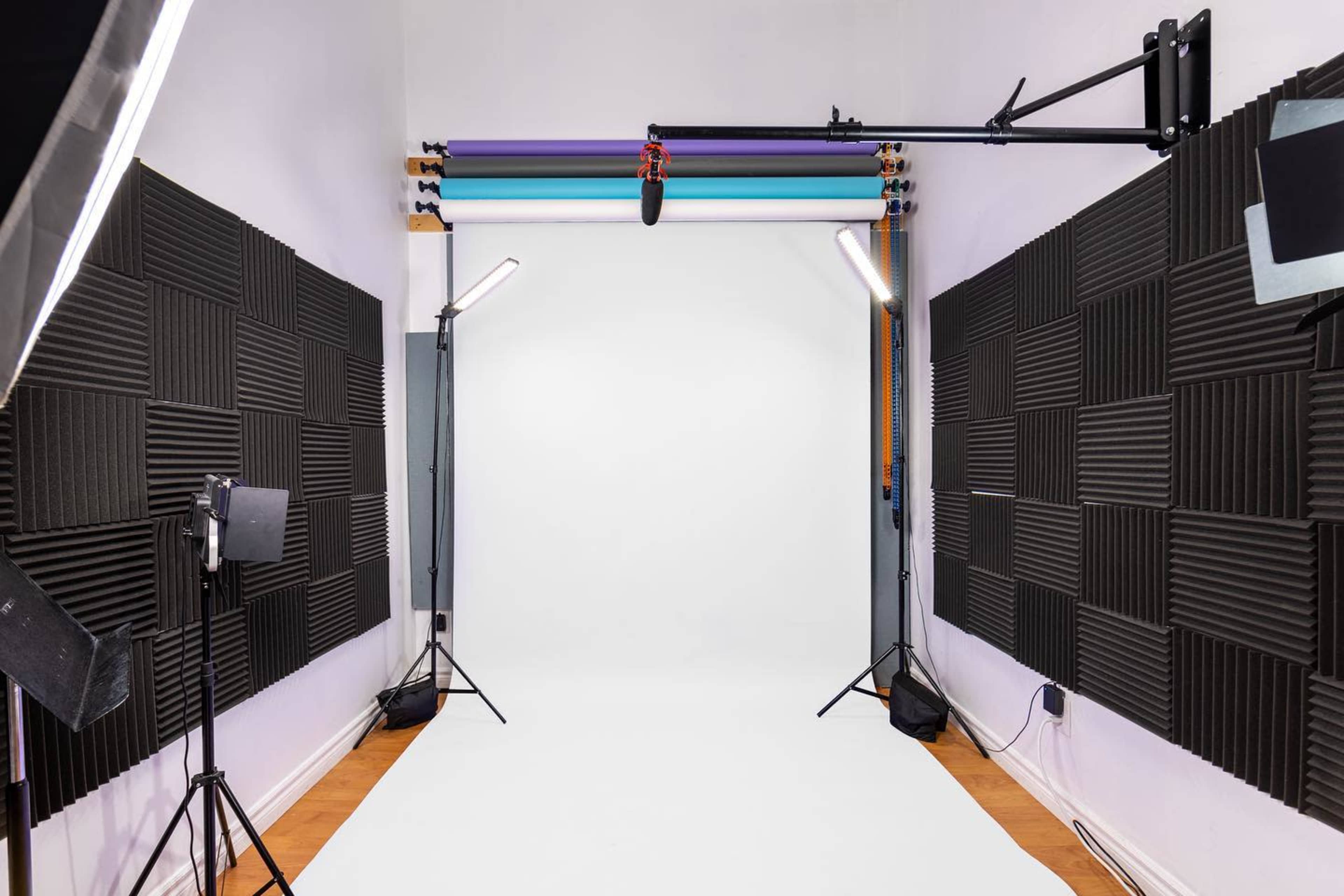 A photography studio with a white backdrop, soundproofing panels on the walls, and lighting equipment set up for a shoot.