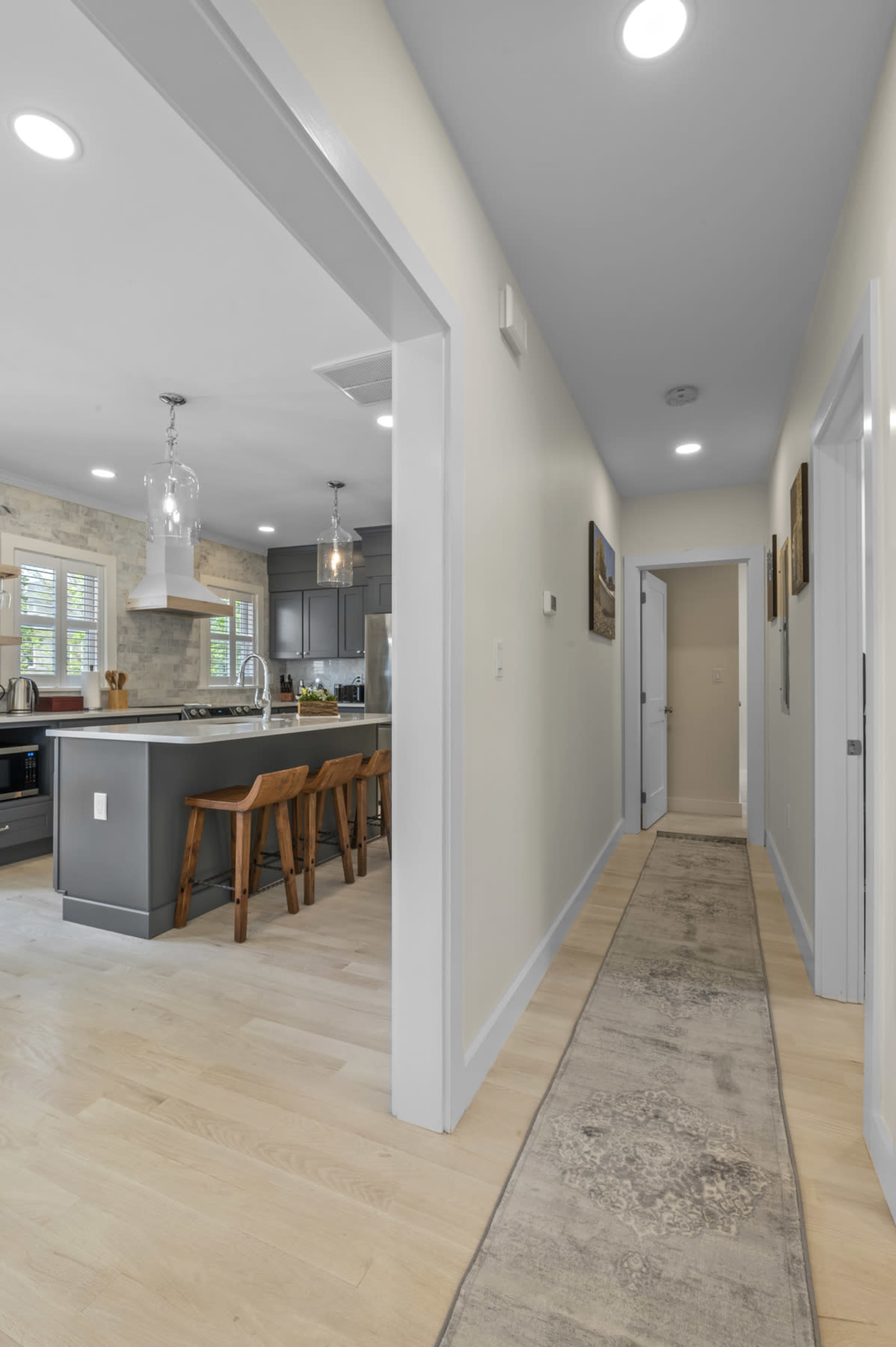 A hallway leads to a kitchen with a central island and seating, featuring modern cabinets and appliances.