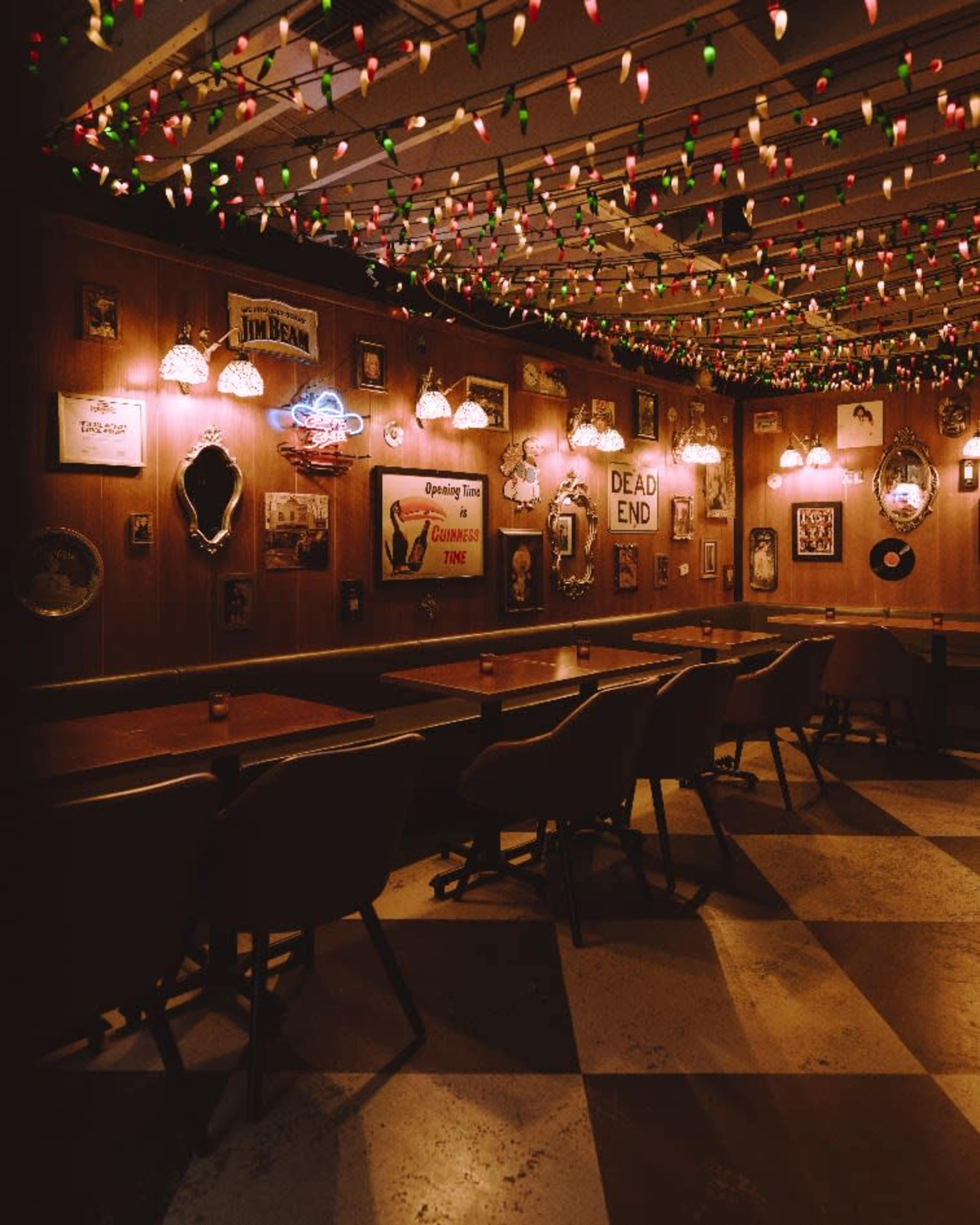 The image shows a cozy bar interior adorned with colorful string lights and various framed decorations on the walls.