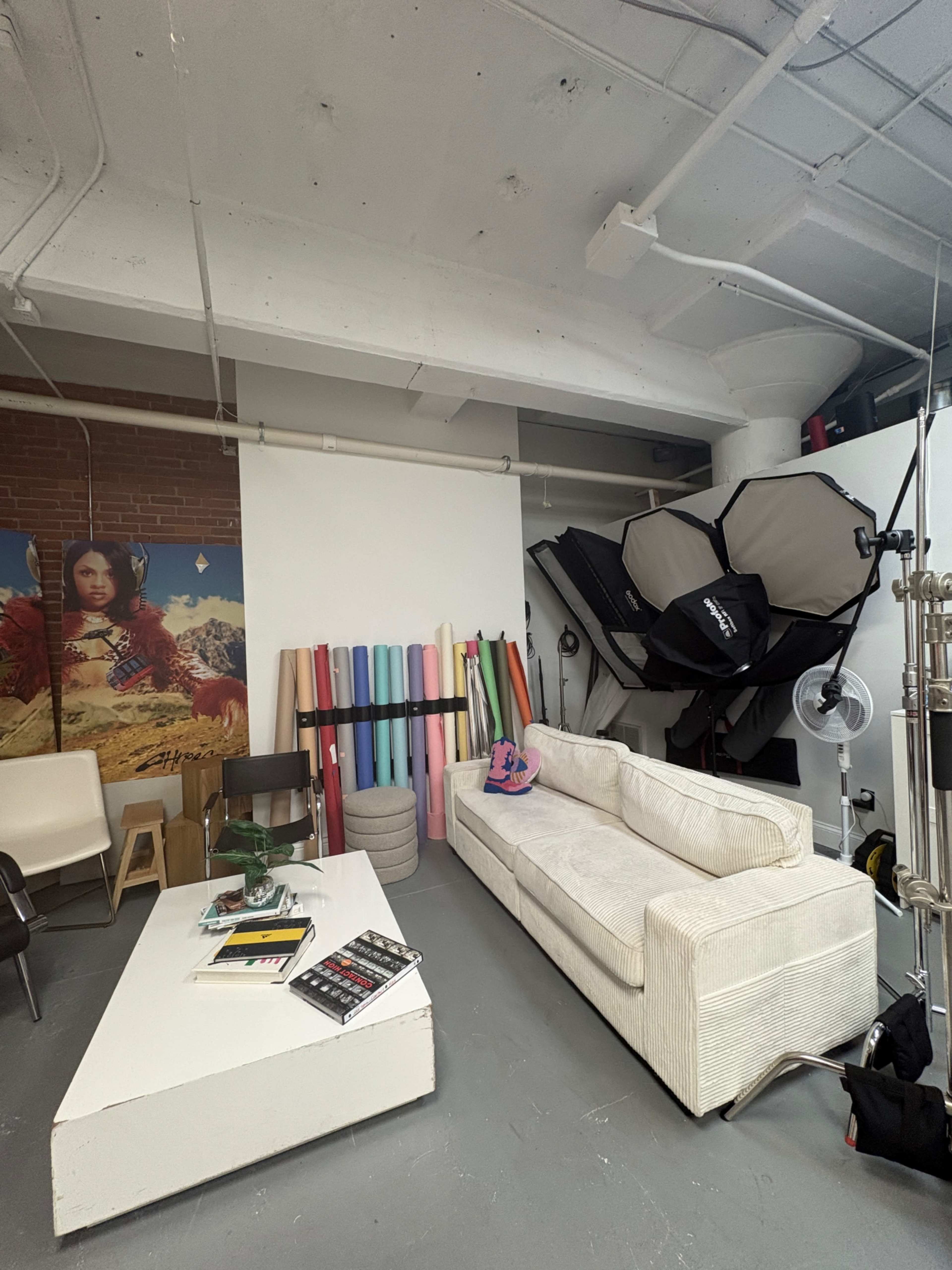 The image shows a studio space featuring a white sofa, a coffee table with magazines, colorful backdrop rolls against the wall, and professional lighting equipment.