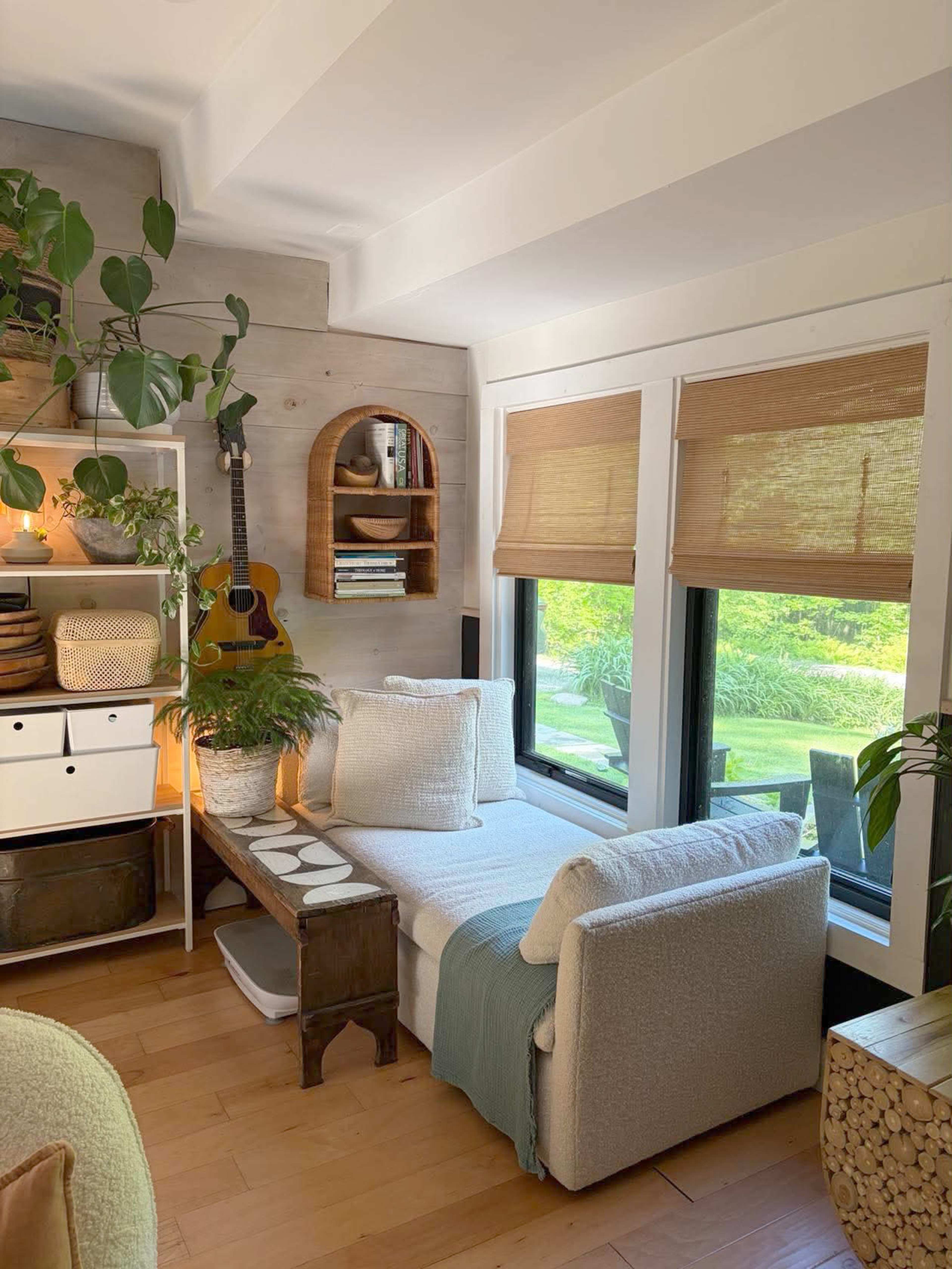 The image shows a cozy living space featuring a fitted window seat, houseplants, a bookshelf, and a guitar against the wall.