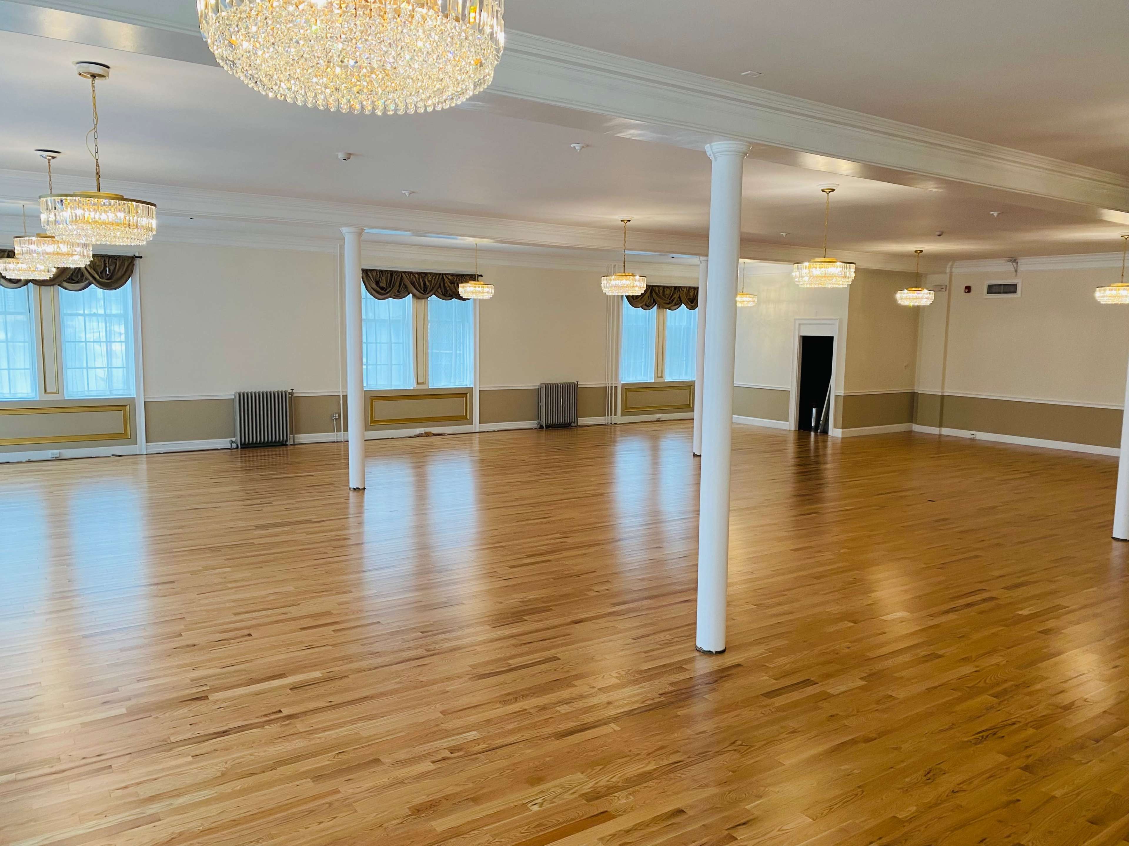 A spacious room with polished wooden floors, white walls, and several chandeliers hanging from the ceiling.
