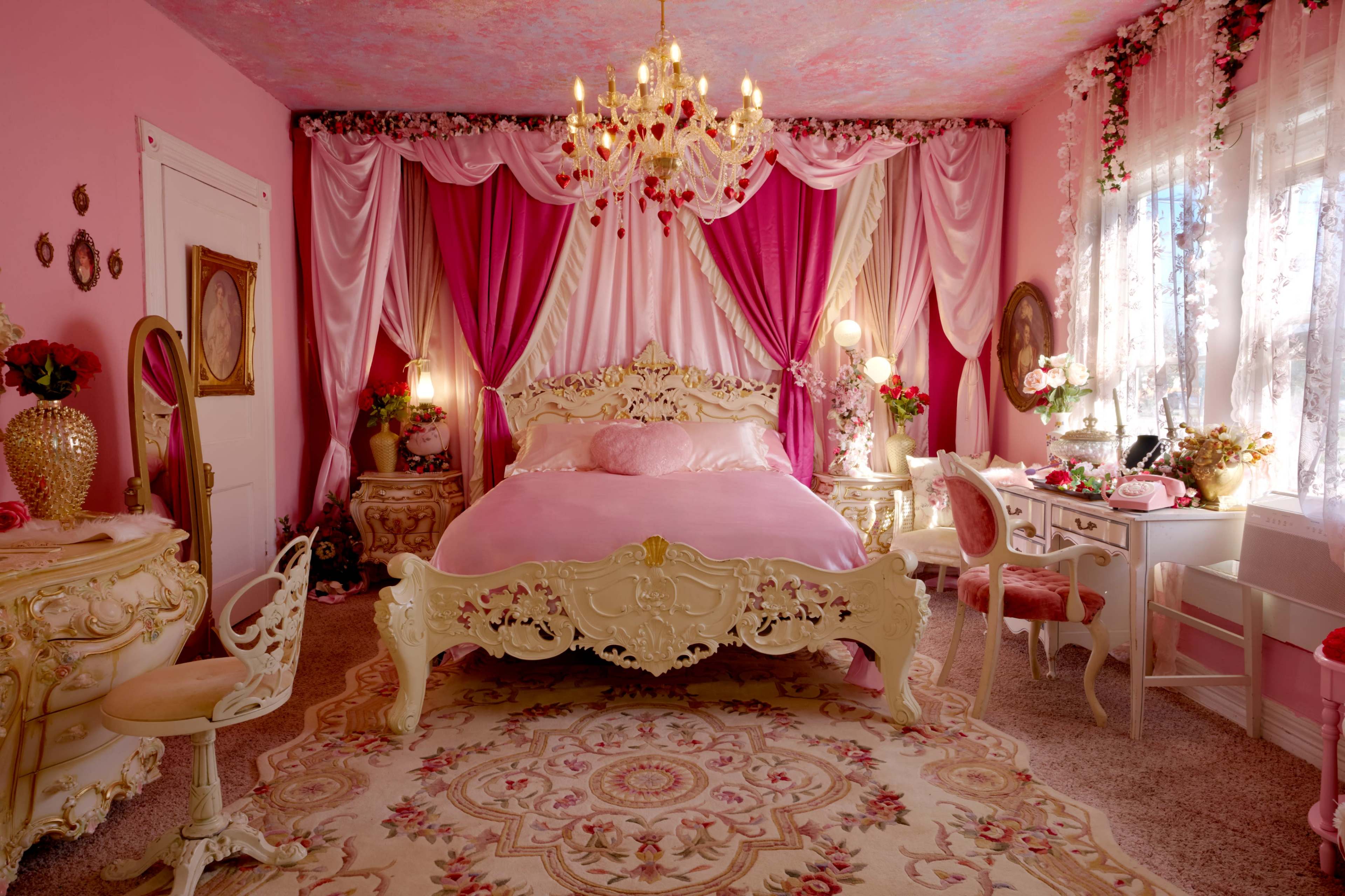 The image shows a lavishly decorated pink bedroom with an ornate bed, matching furniture, and intricate drapery.