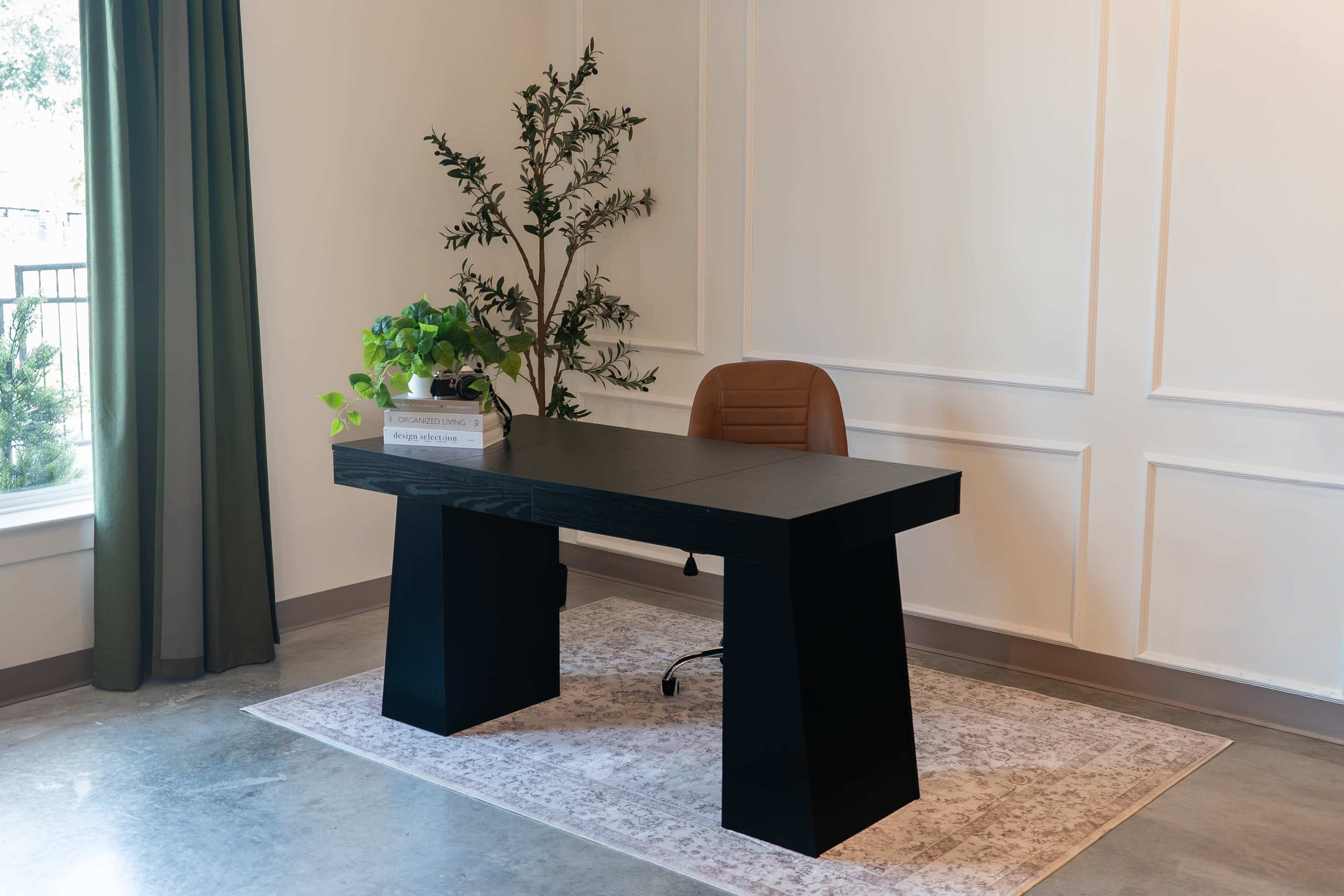 A modern black desk with a brown leather chair sits in a well-lit room, accompanied by a green plant and a decorative box on the desk.