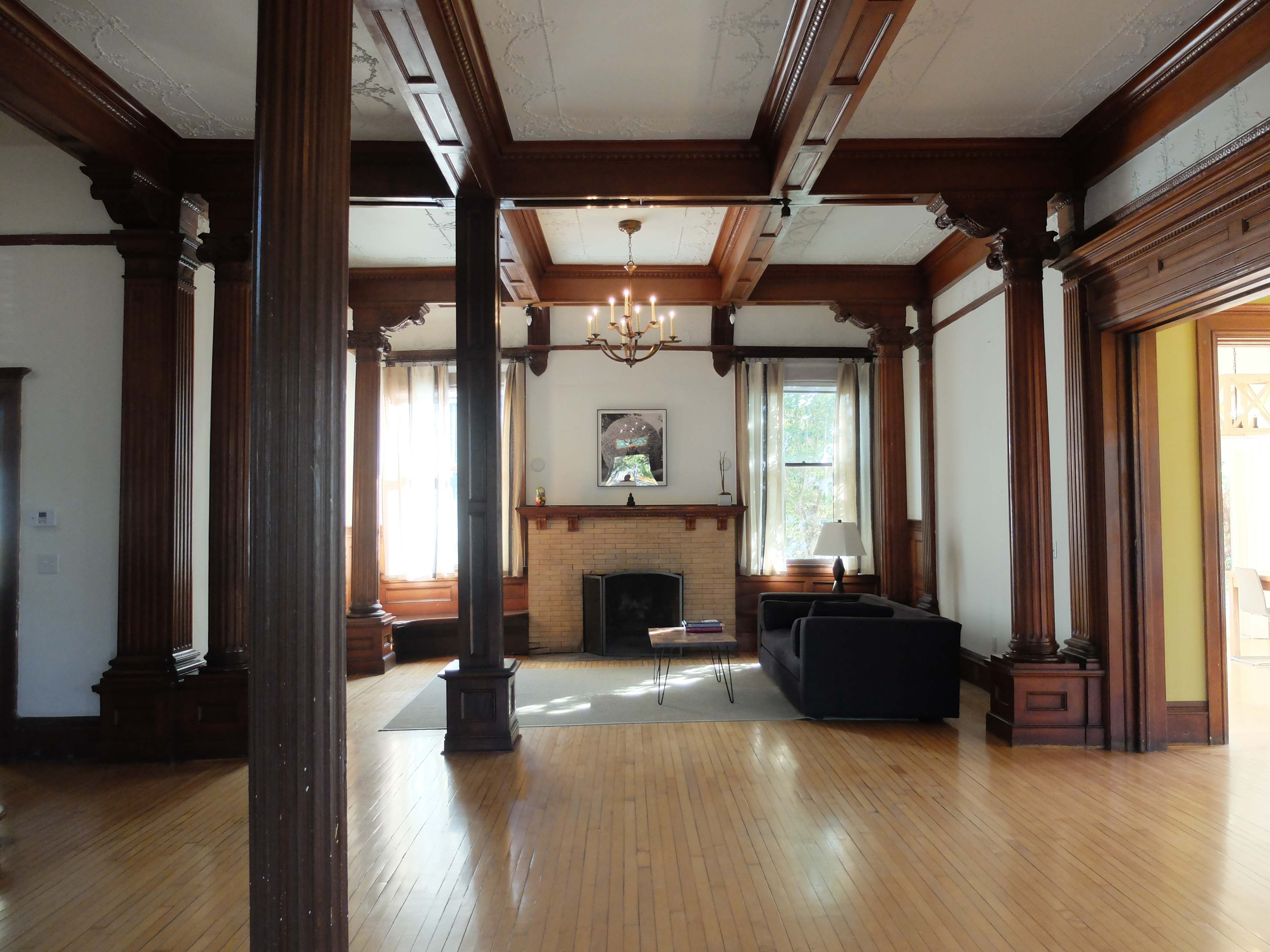 A spacious living room with wooden pillars, a fireplace, and large windows allowing natural light to enter.