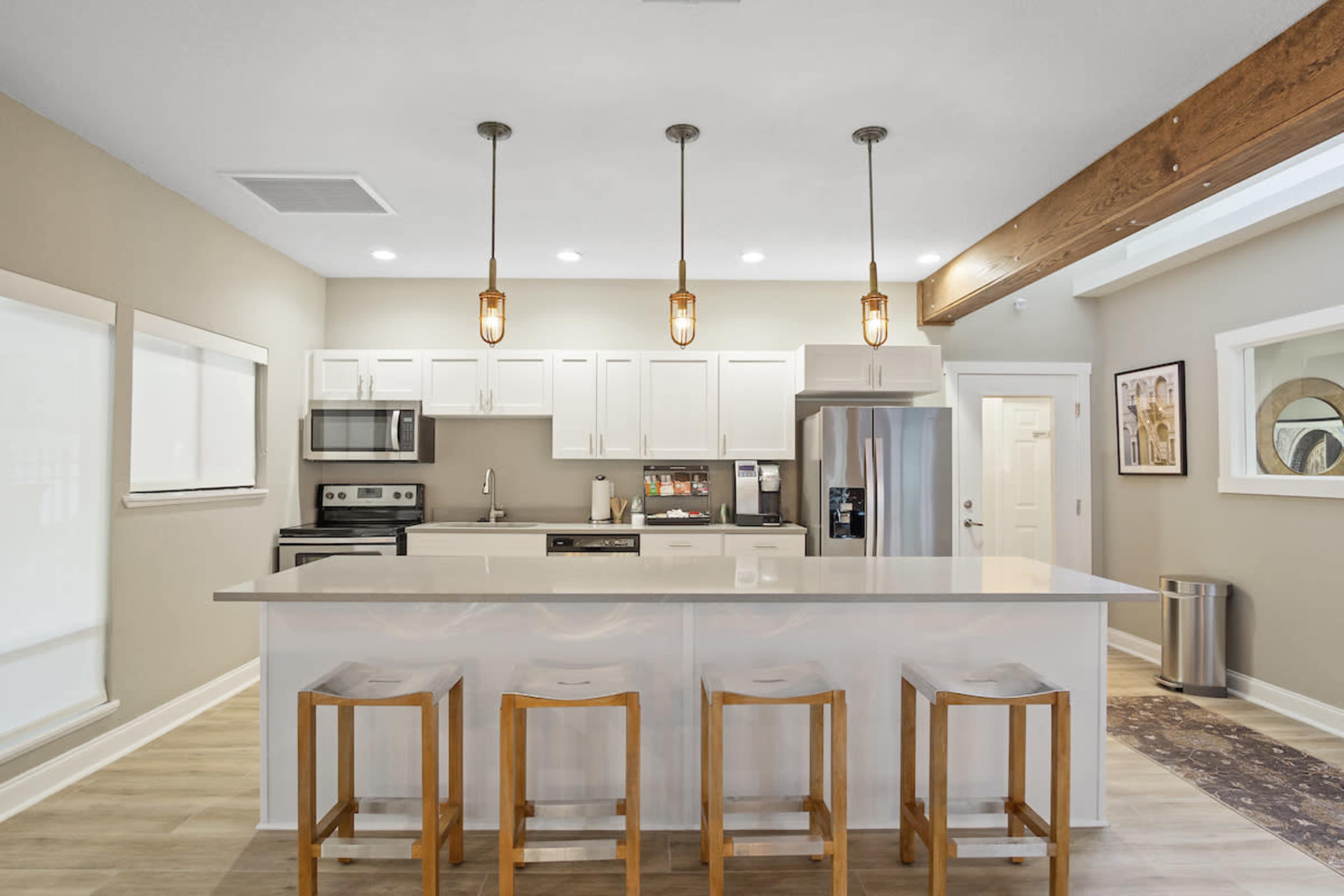 A modern kitchen features white cabinetry, stainless steel appliances, and a central island with four wooden barstools.