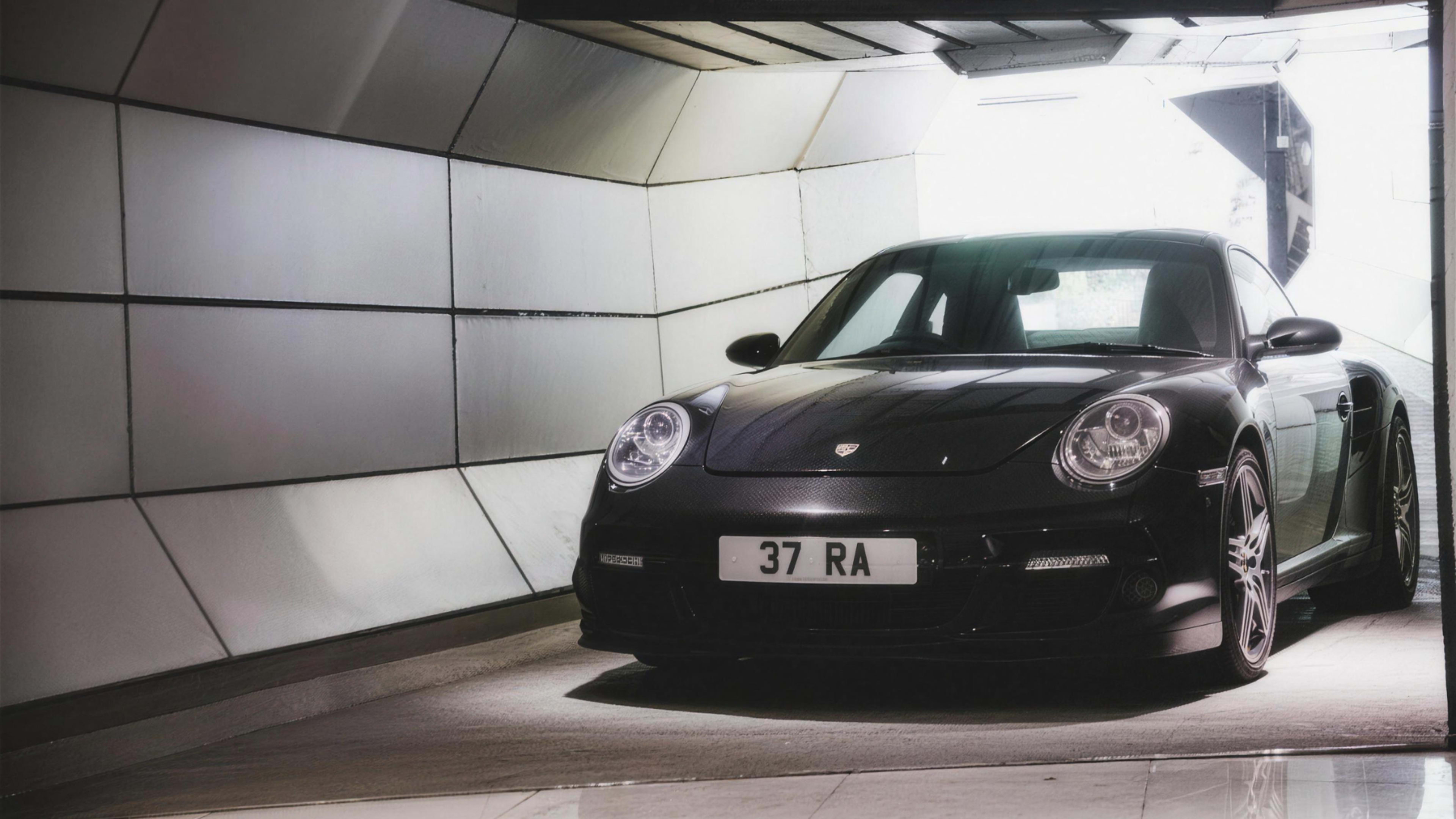 A black Porsche 911 is parked in a modern tunnel with a bright exit at the end.