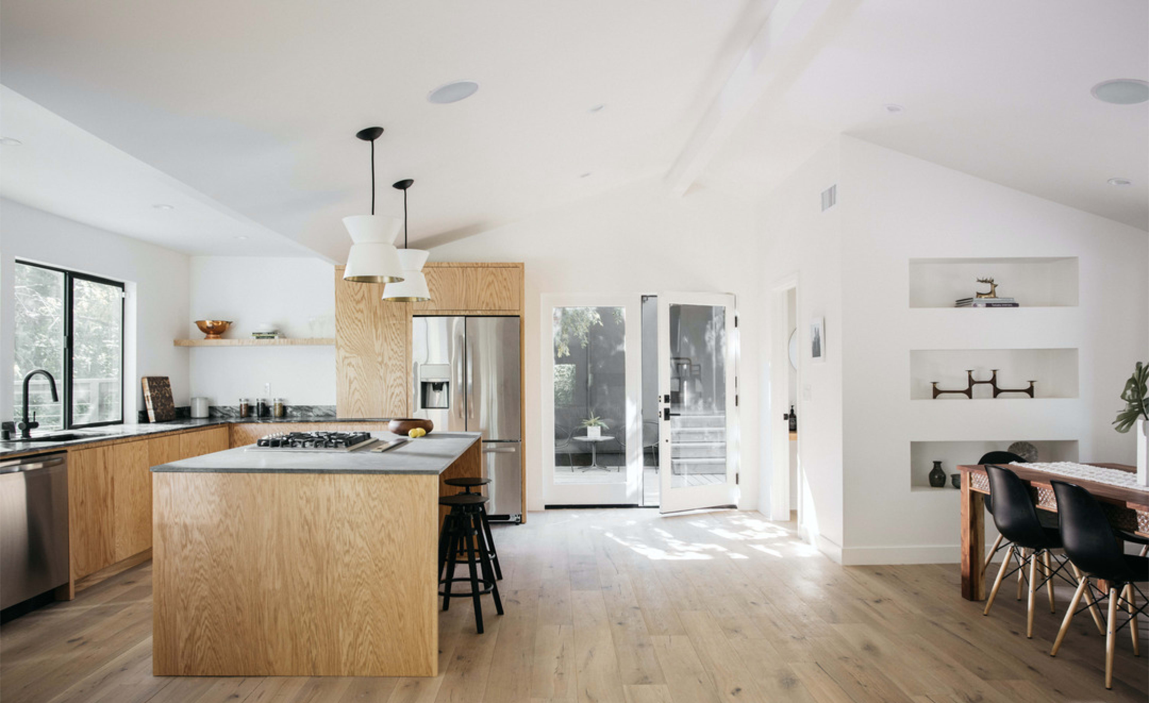 A modern kitchen features a large island with wooden cabinets, stainless steel appliances, and an adjacent dining area with a wooden table.