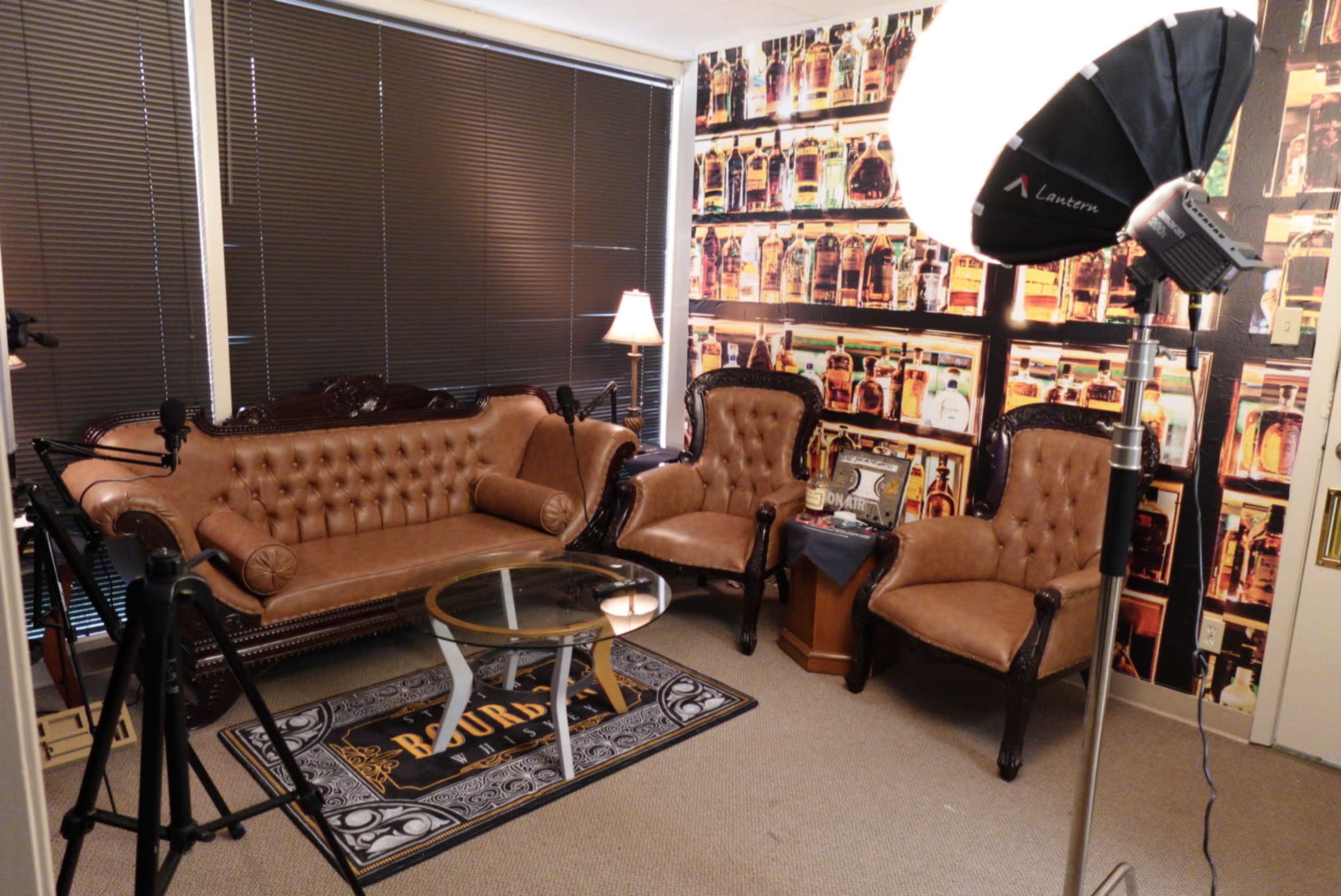 A small room furnished with a brown leather sofa, two matching armchairs, a glass coffee table, and a backdrop of a wall covered in a patterned wallpaper featuring images of bottles.