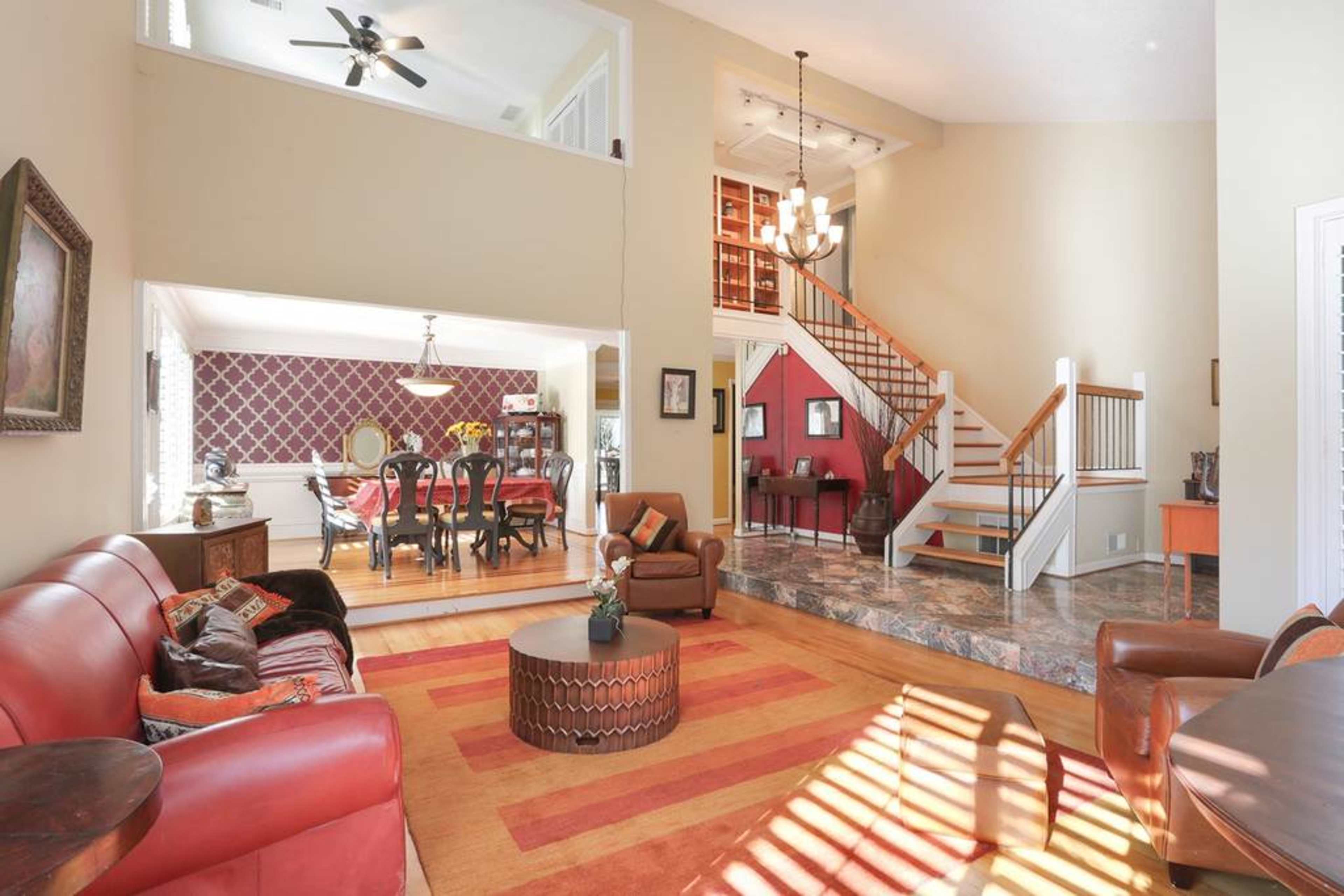 A spacious living area featuring leather sofas, a coffee table, and a staircase leading to an upper level, with a dining area visible in the background.