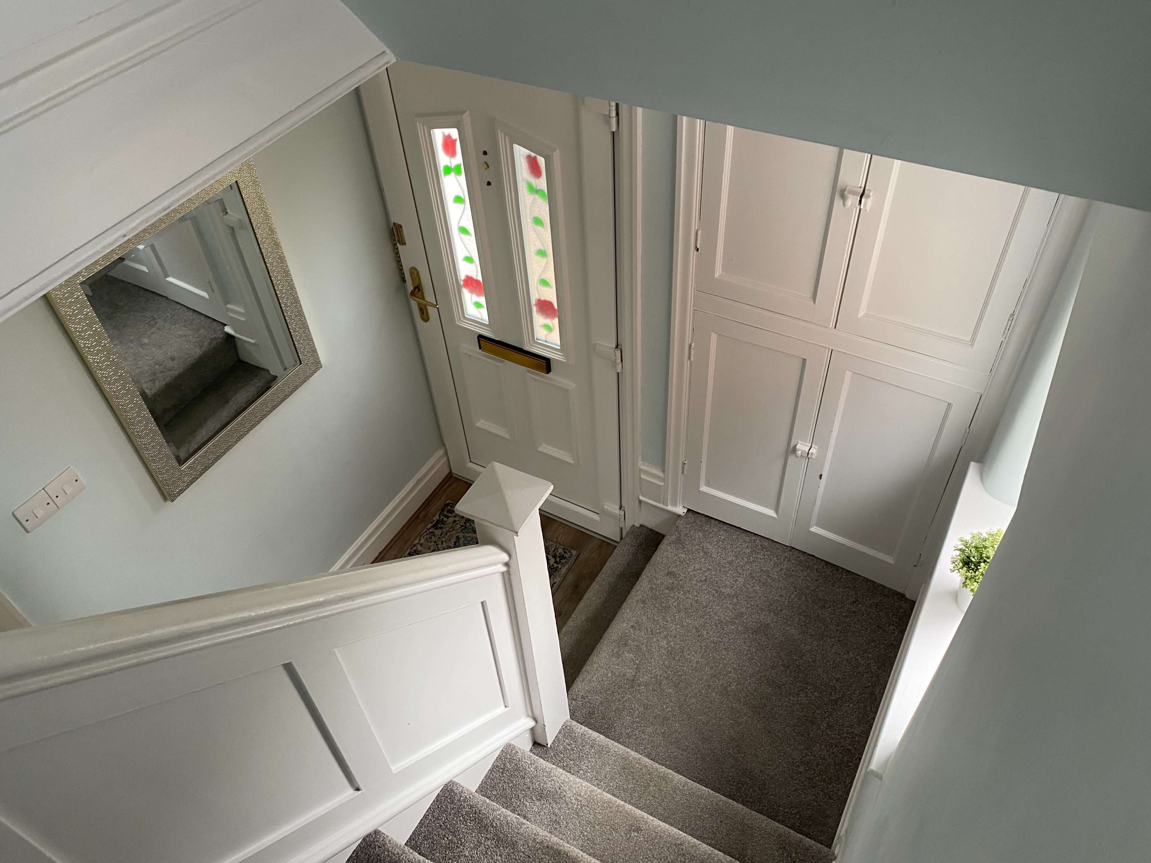 A stairway leading to a glass-paneled front door, with a mirror on the wall and closed cabinets nearby.