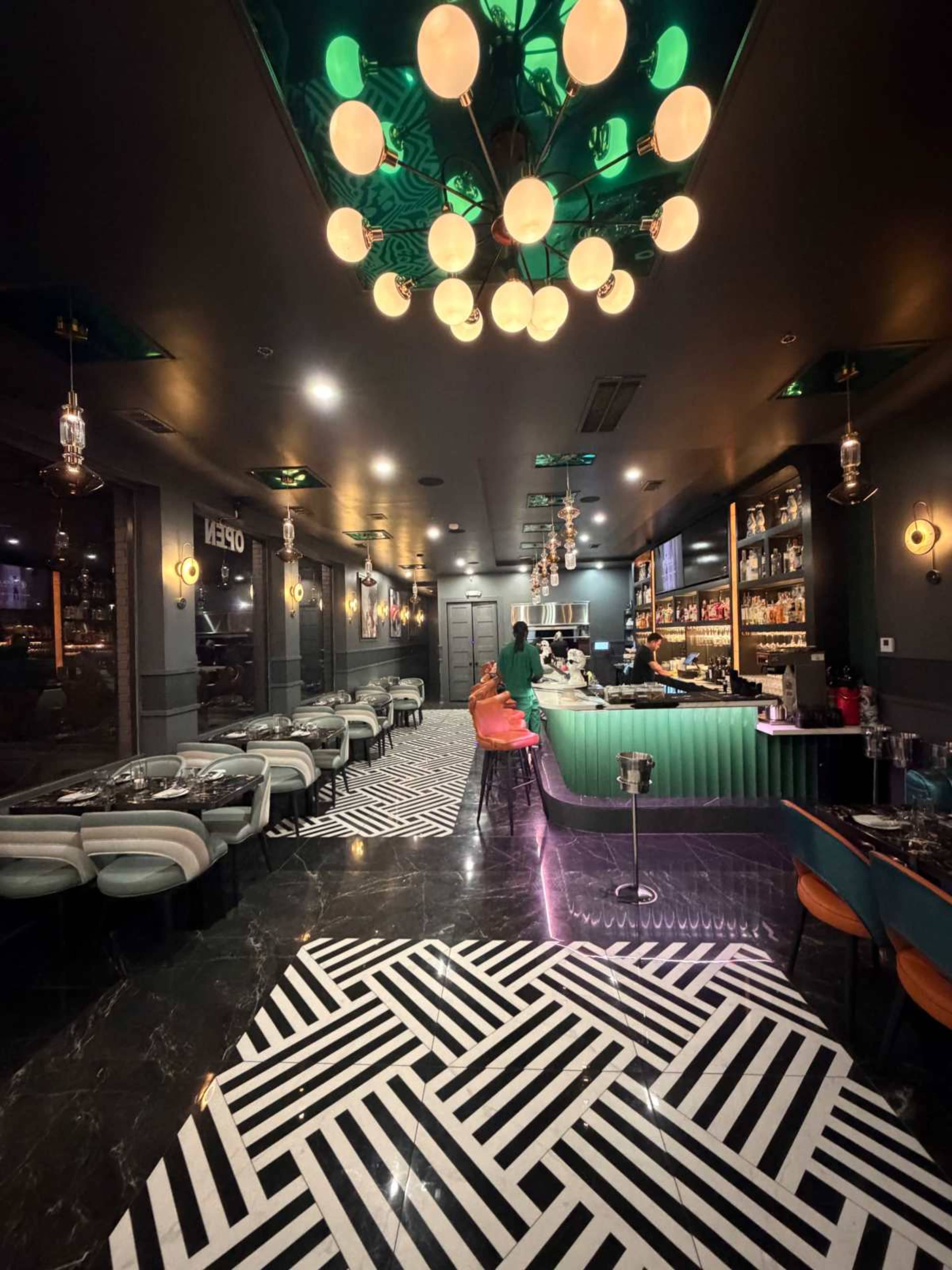 The image shows a modern restaurant interior with a bar, patterned flooring, and a mix of seating arrangements.
