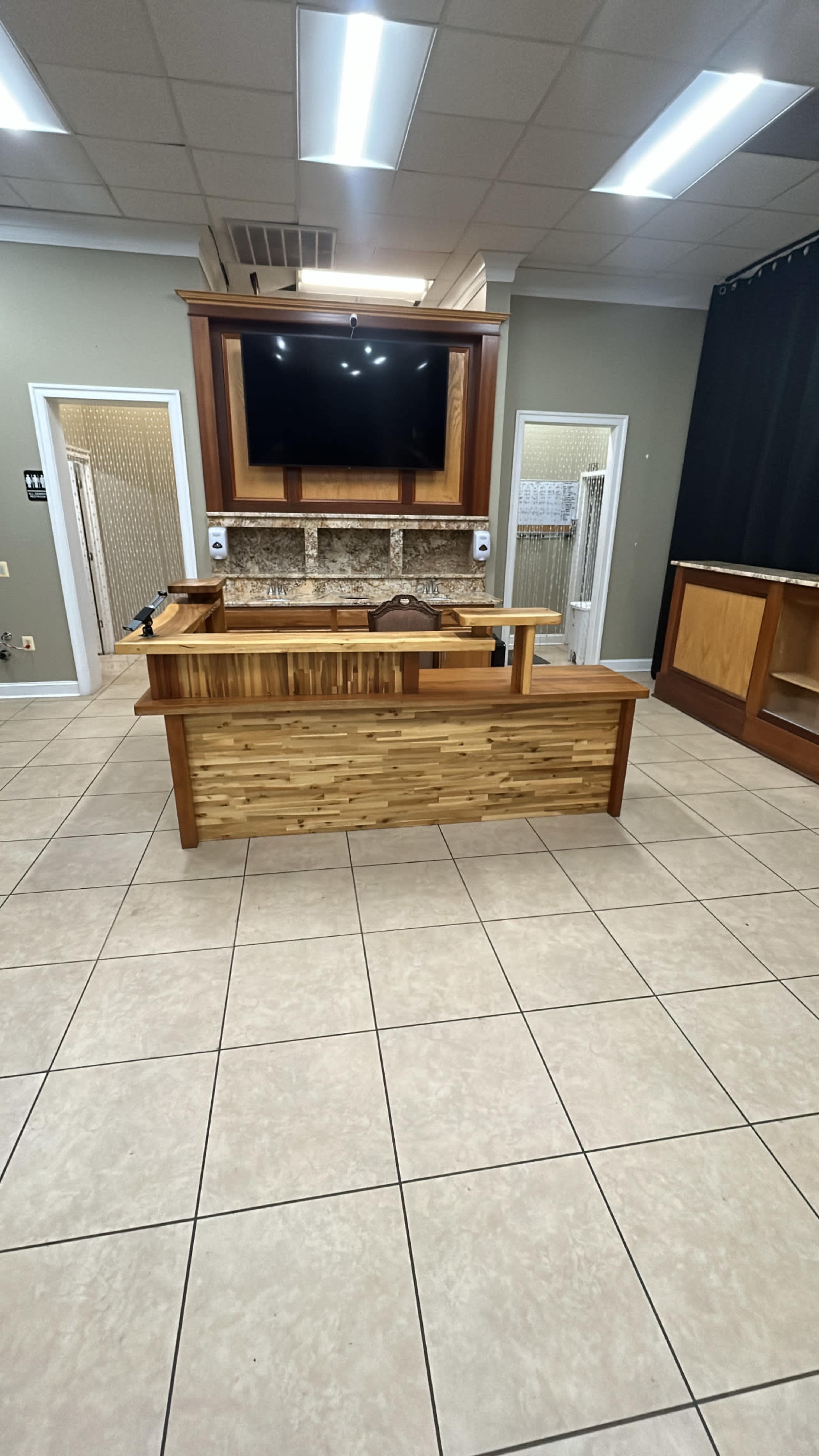 A modern reception area with a wooden reception desk, a large flat-screen TV mounted above it, and tiled flooring.