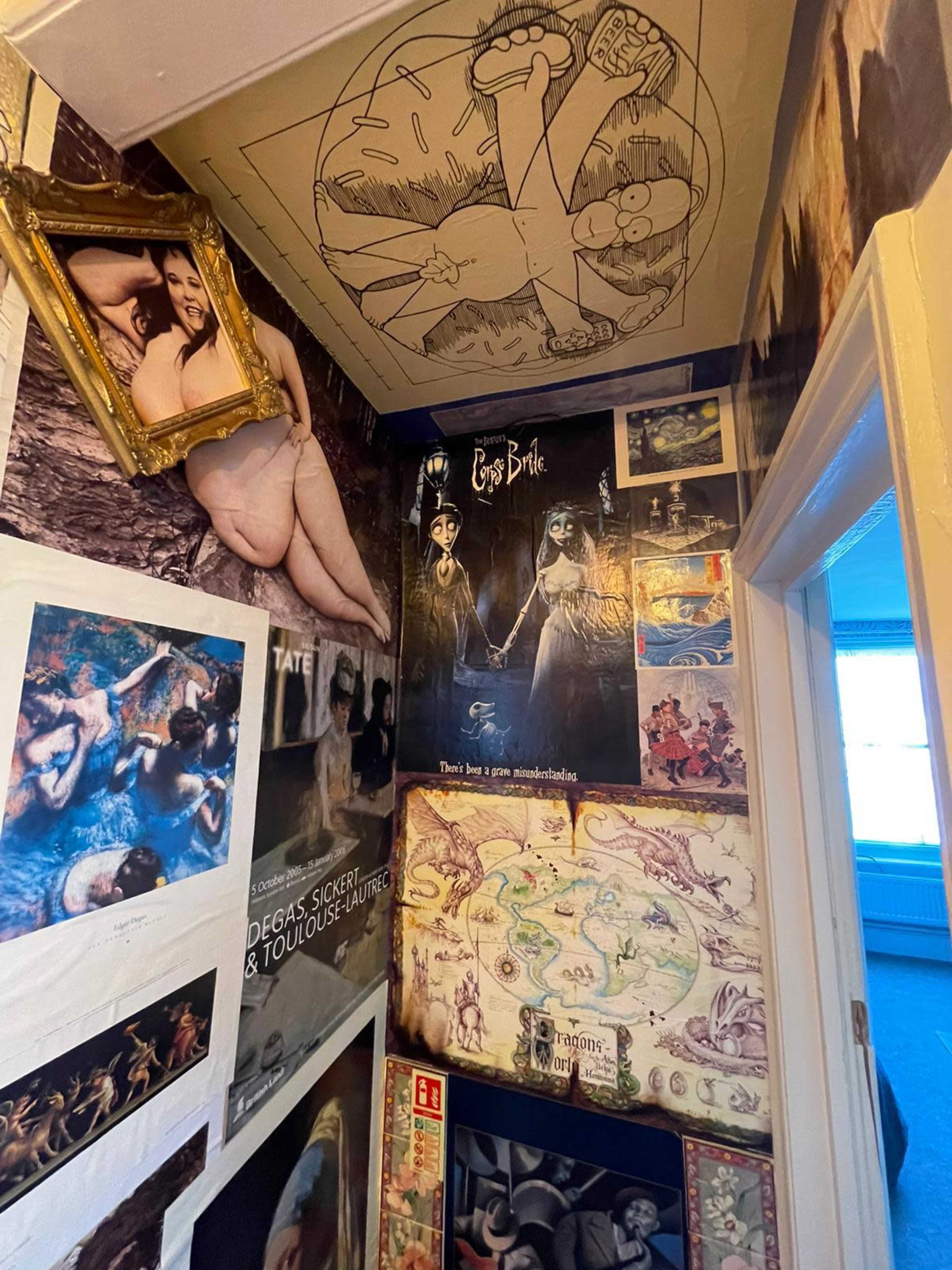 The image shows a narrow hallway adorned with a variety of posters, photographs, and artwork, including a ceiling mural and a framed piece on the wall.