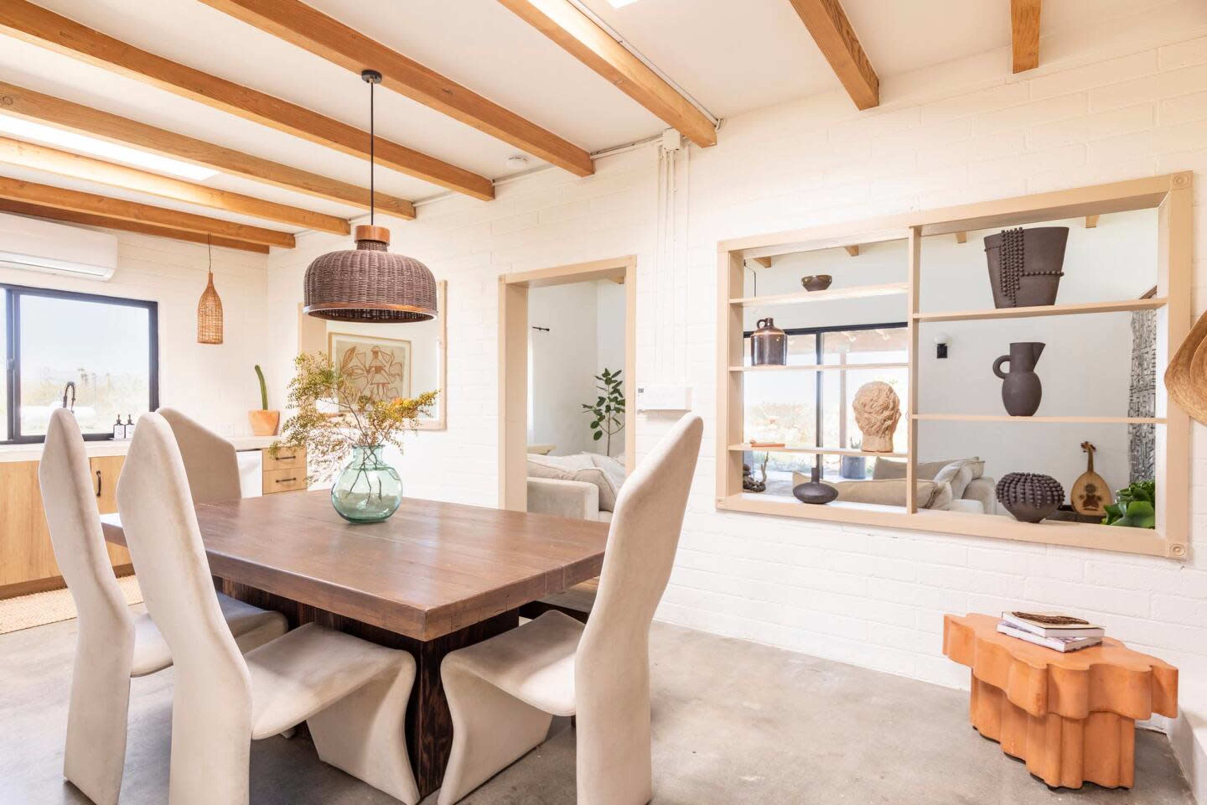 A spacious dining area features a wooden table surrounded by upholstered chairs, with large windows and exposed beams overhead.