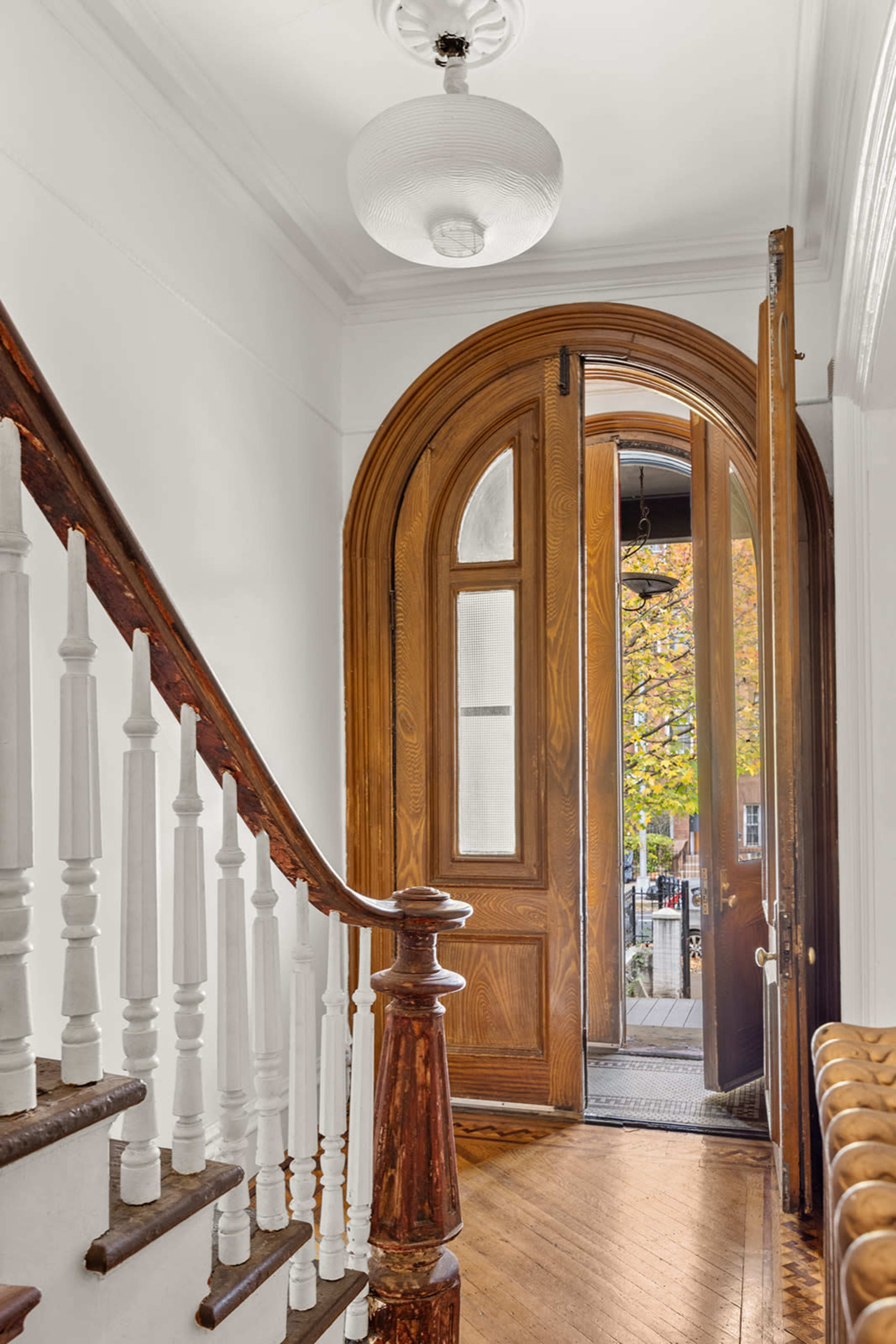 A wooden staircase leads to an arched doorway, which opens to a view of an outdoor area with trees.