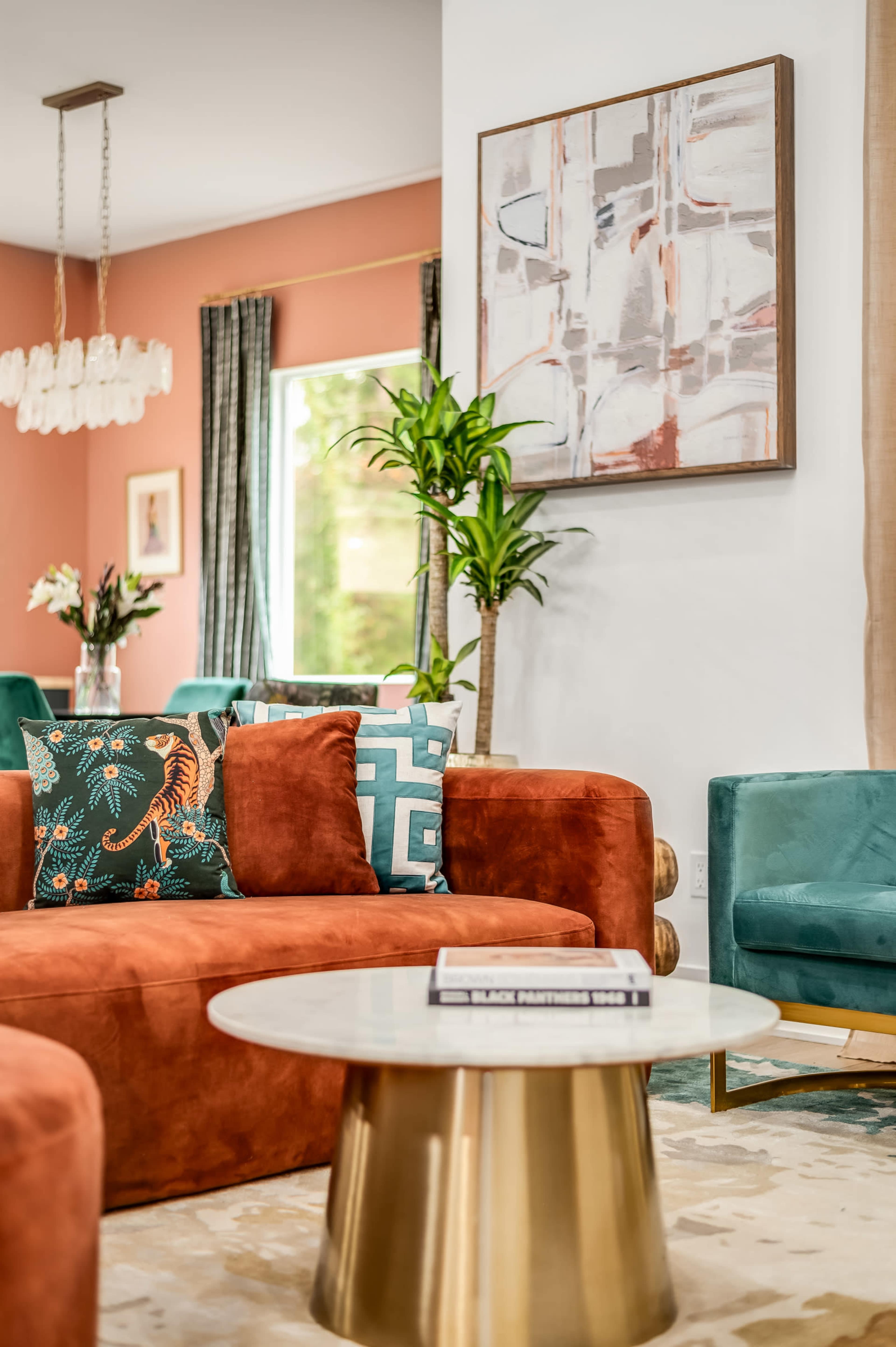 The image shows a stylish living room featuring an orange sectional sofa with colorful pillows, a round coffee table, and a large abstract painting on the wall.