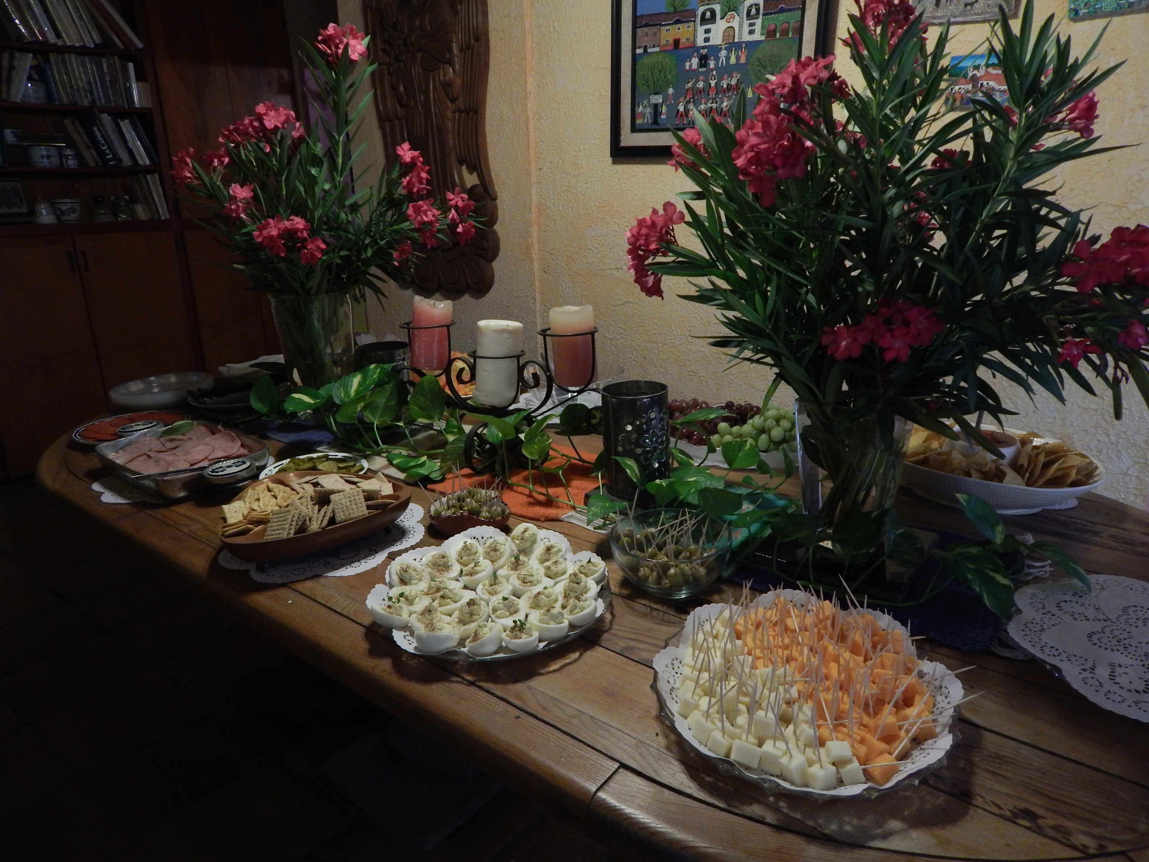 A wooden table set with various platters of food, including meats, cheeses, crackers, and decorative flowers in vases.