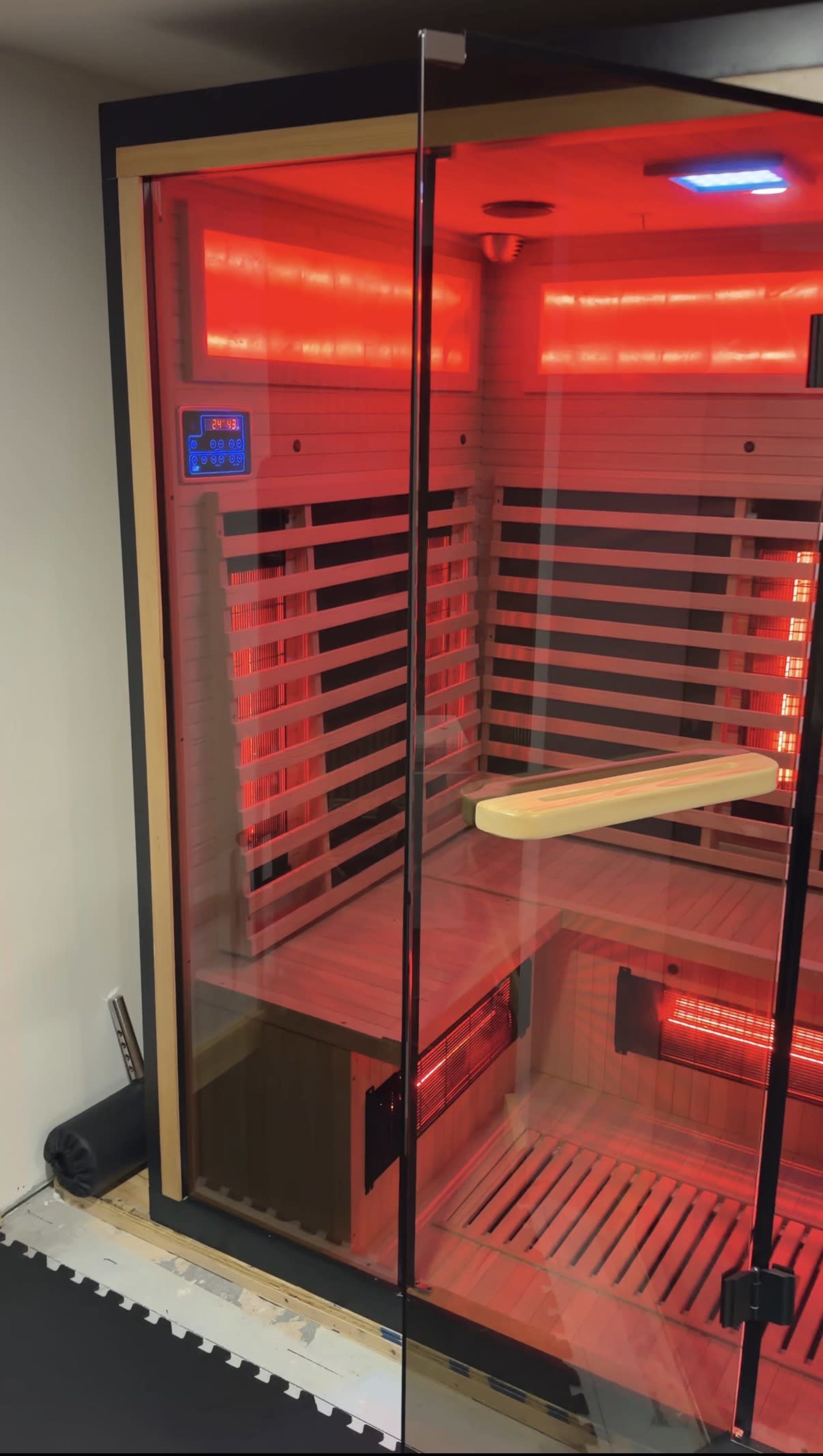 The image shows a wooden infrared sauna with red lighting and a glass door.