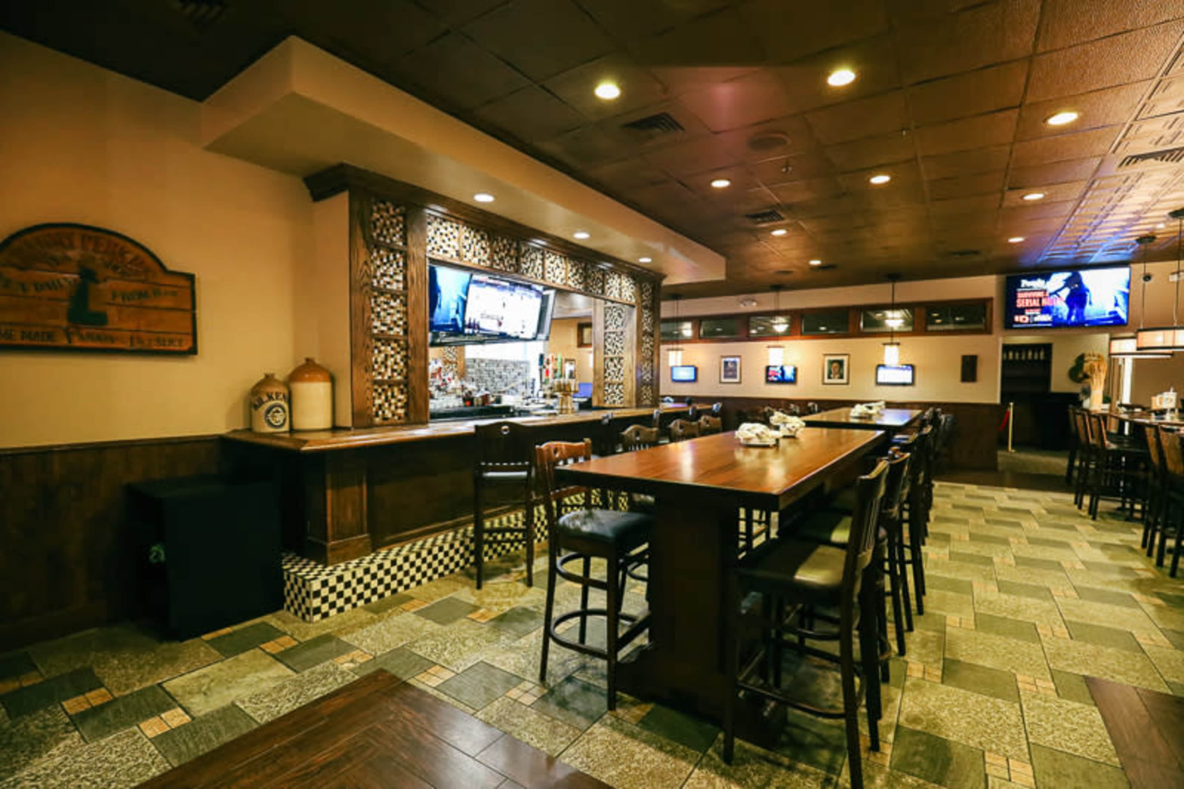 The interior of a restaurant with a bar area featuring wooden furniture, tiled flooring, and several televisions mounted on the walls.