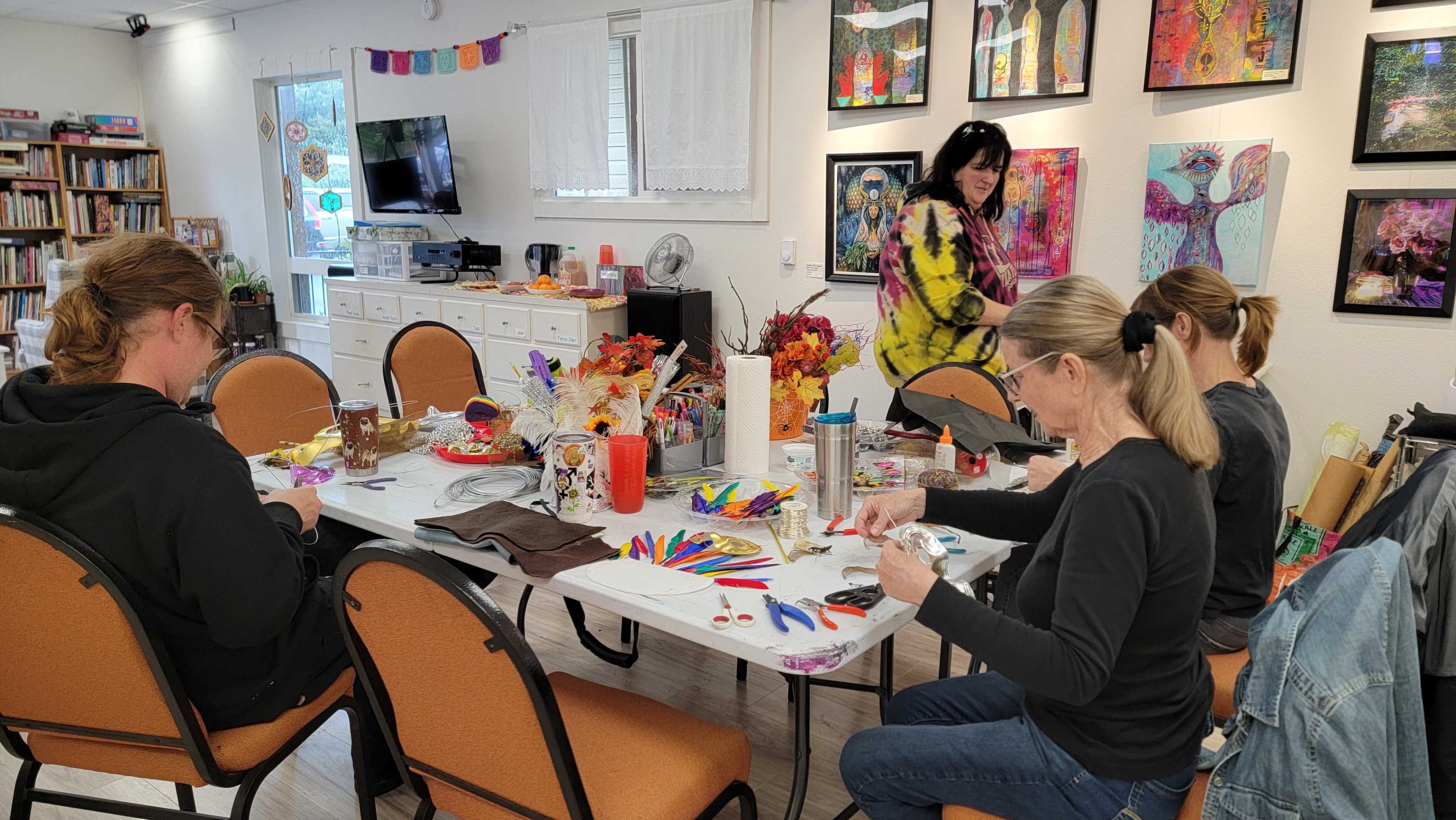 A group of four people participates in an arts and crafts activity at a table adorned with various supplies in a colorful room decorated with artwork.