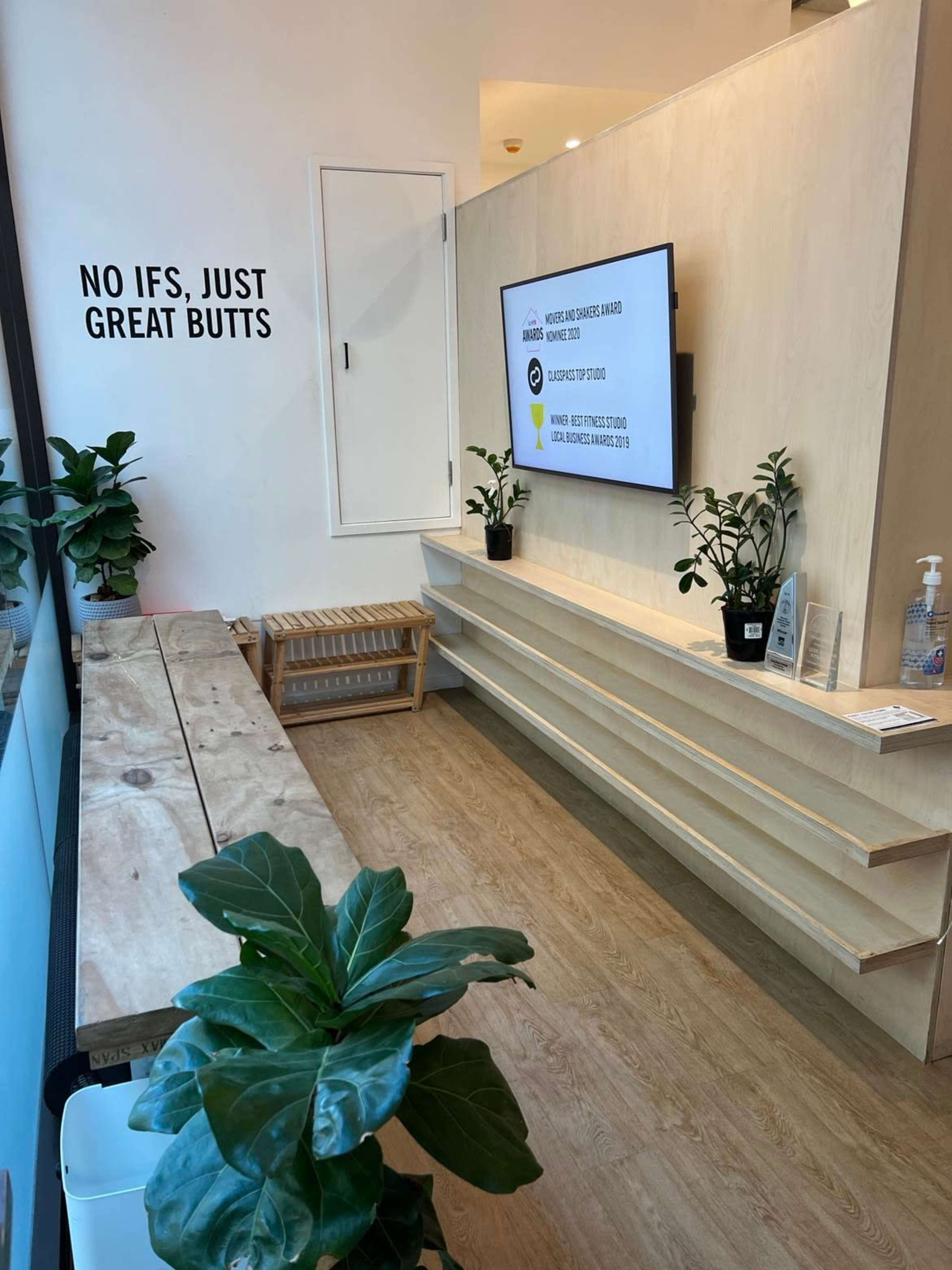 A modern waiting area with a wooden bench, potted plants, and a television mounted on the wall displaying a message.
