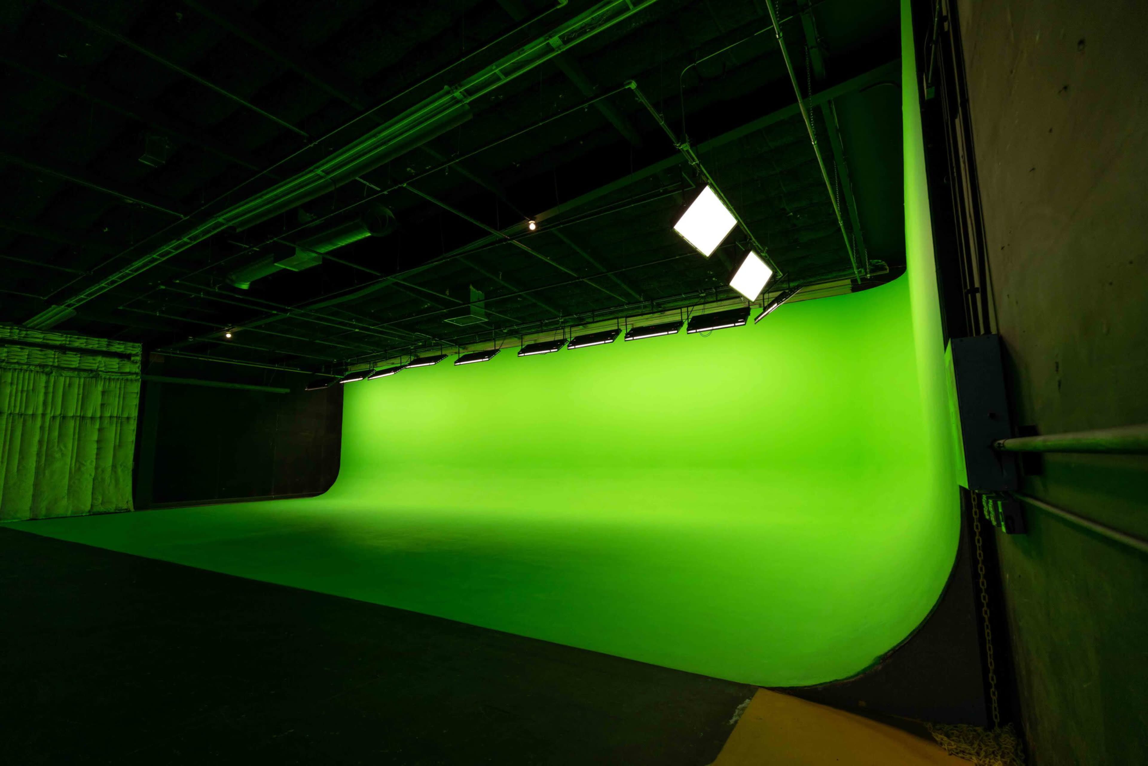 The image shows a green screen studio with a bright green backdrop and overhead lighting.