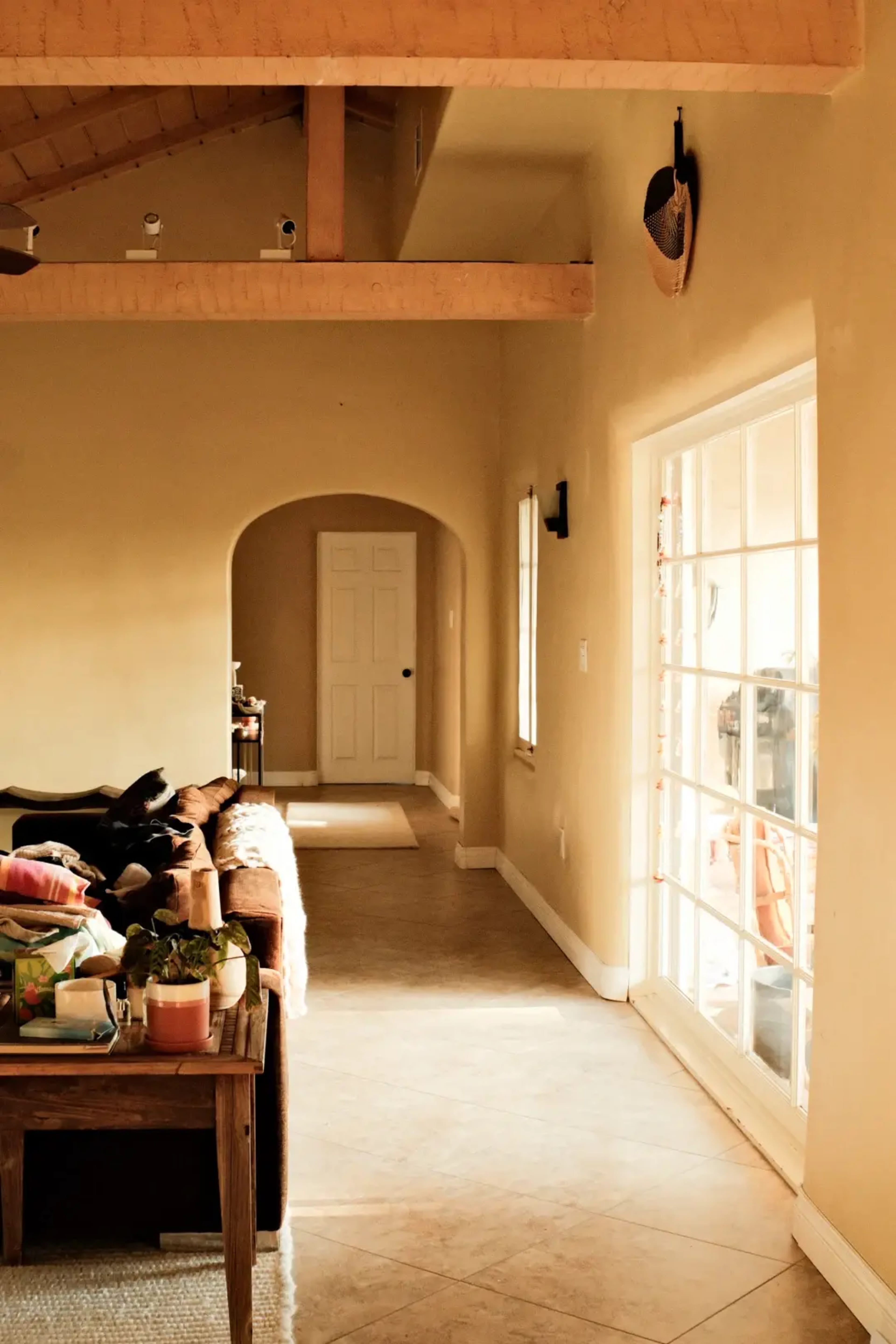 A well-lit living room features a couch with several colorful cushions and a hallway leading to a door at the end.