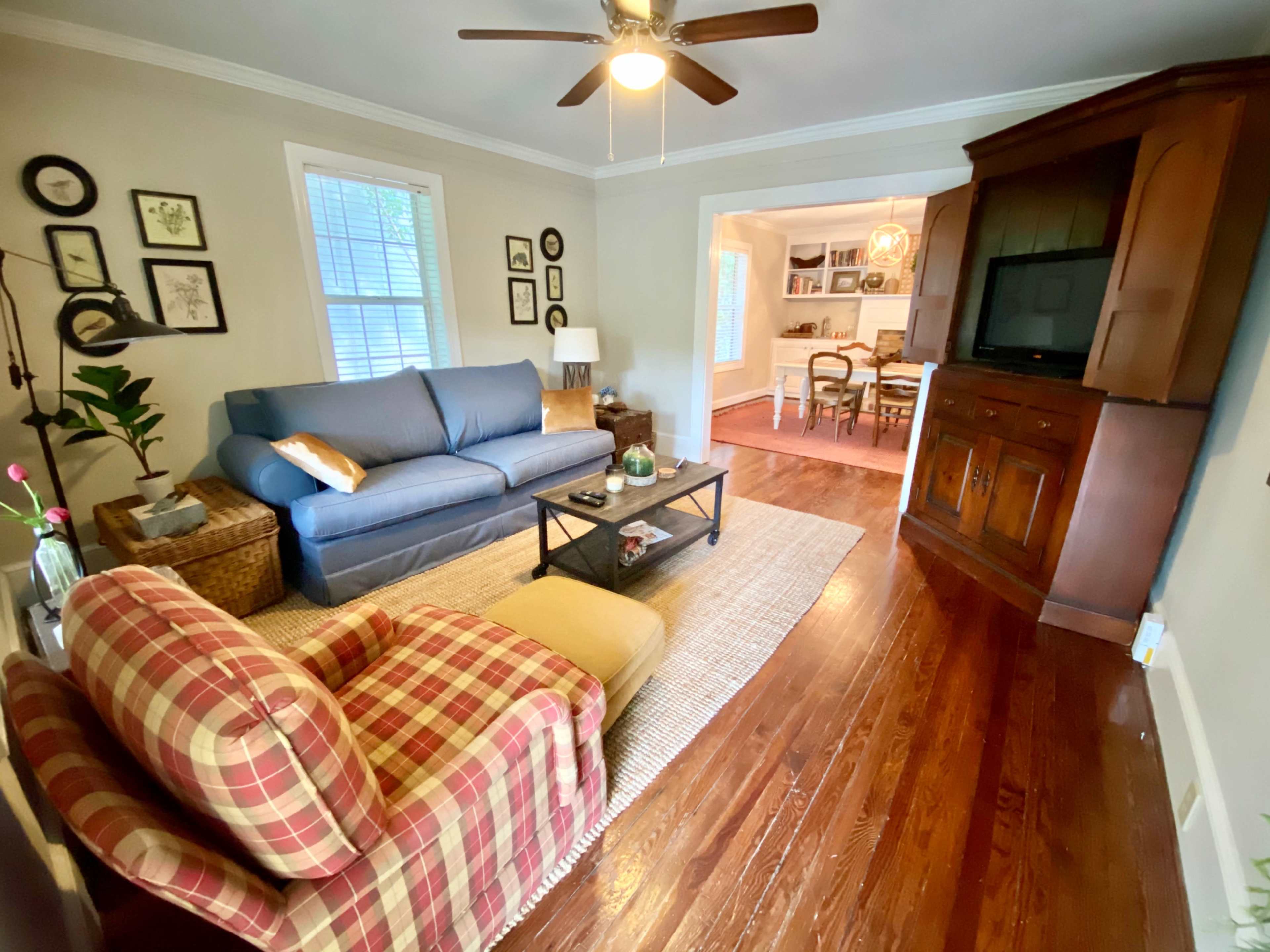 A living room with a blue sofa, a patterned chair, and a wooden TV cabinet, all situated on polished wooden floors.