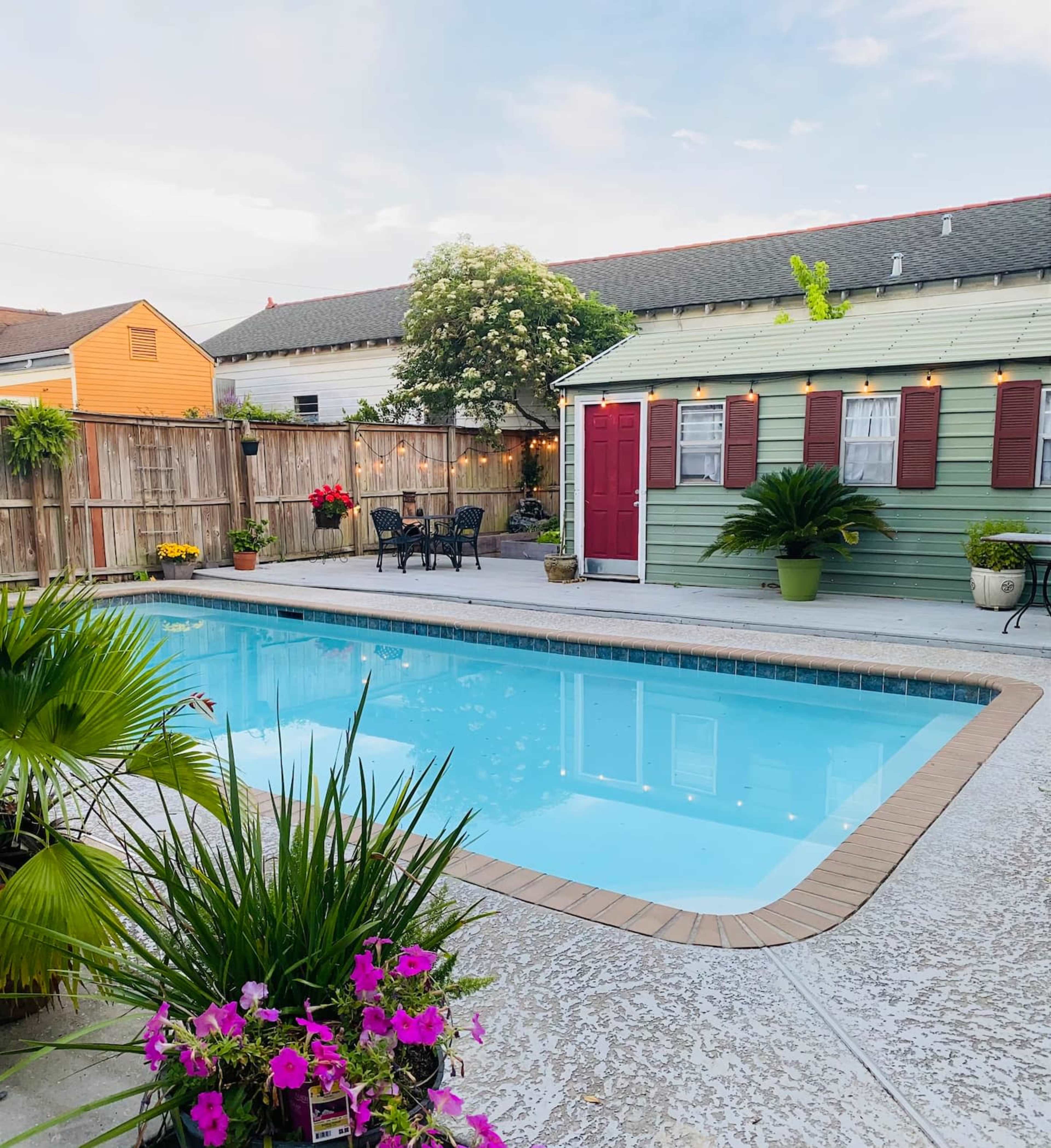 A backyard with a swimming pool surrounded by potted plants and a small shed with a red door.