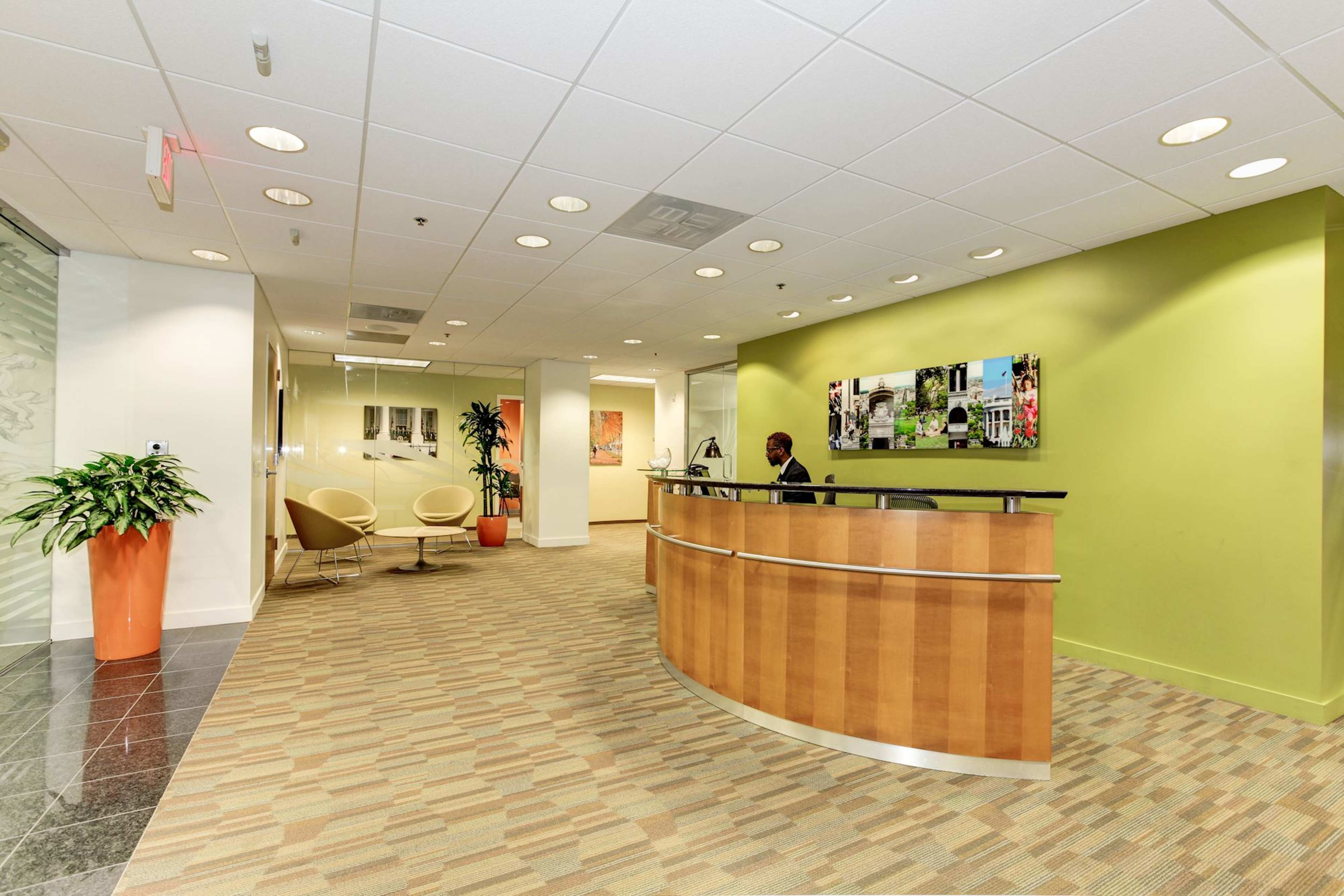 A modern office reception area with a wooden front desk, seating arrangements, and green accent walls.
