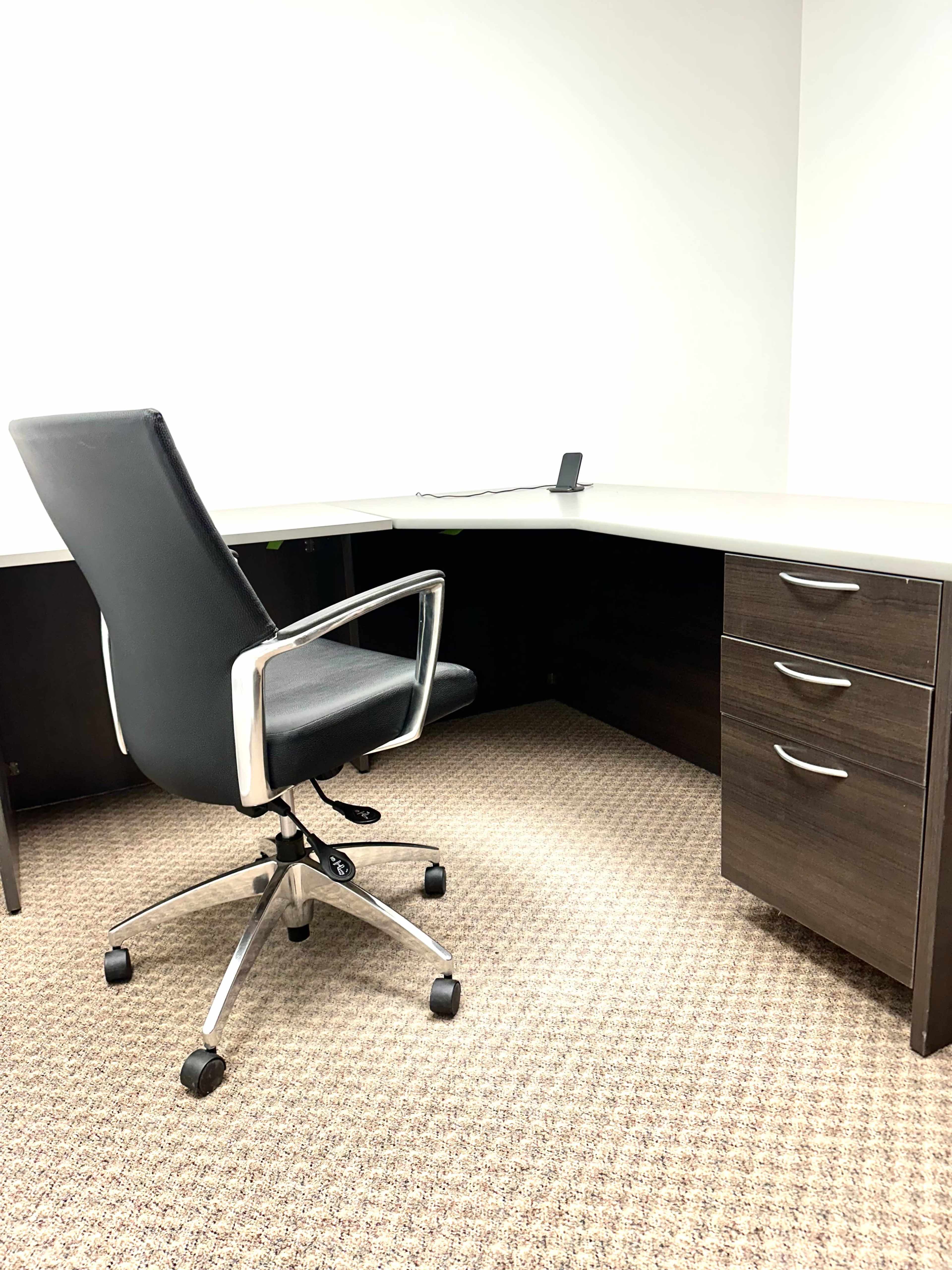An office space with a black swivel chair positioned in front of a desk featuring drawers on the right.