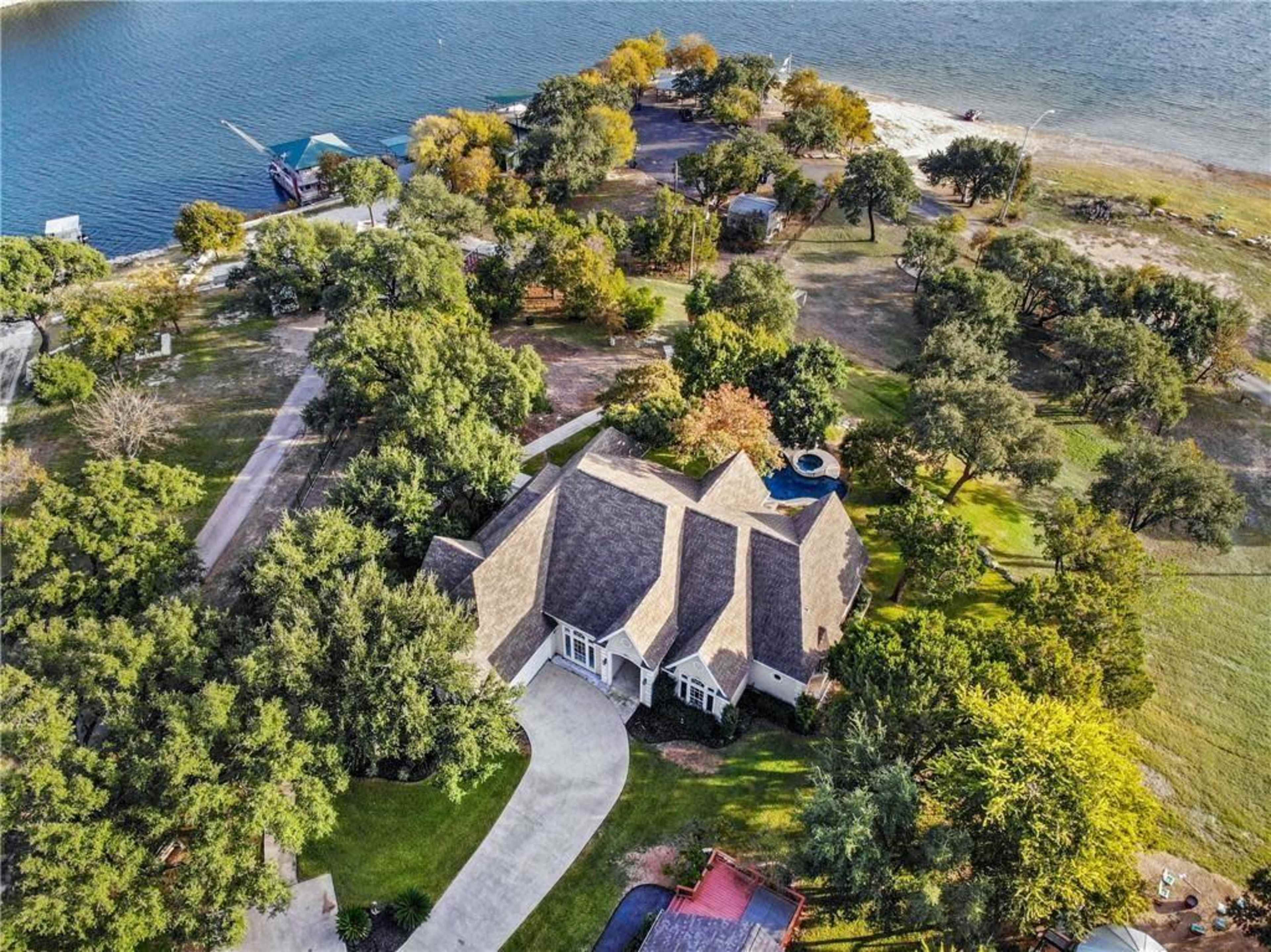 A large house with a brown roof situated near a body of water, surrounded by trees and open land.