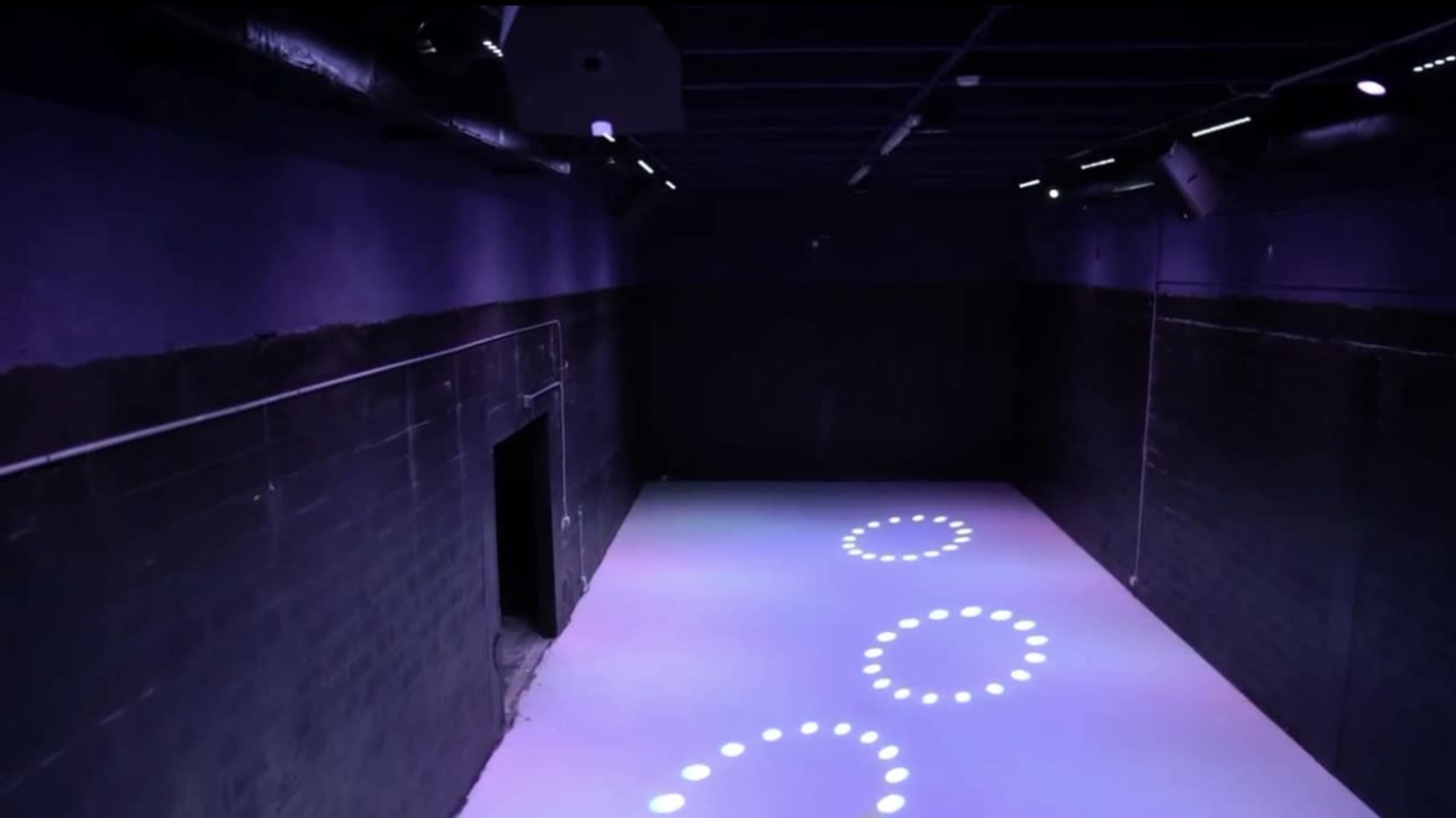 The image shows a dimly lit room with a smooth, white floor illuminated by circular lights arranged in a pattern.