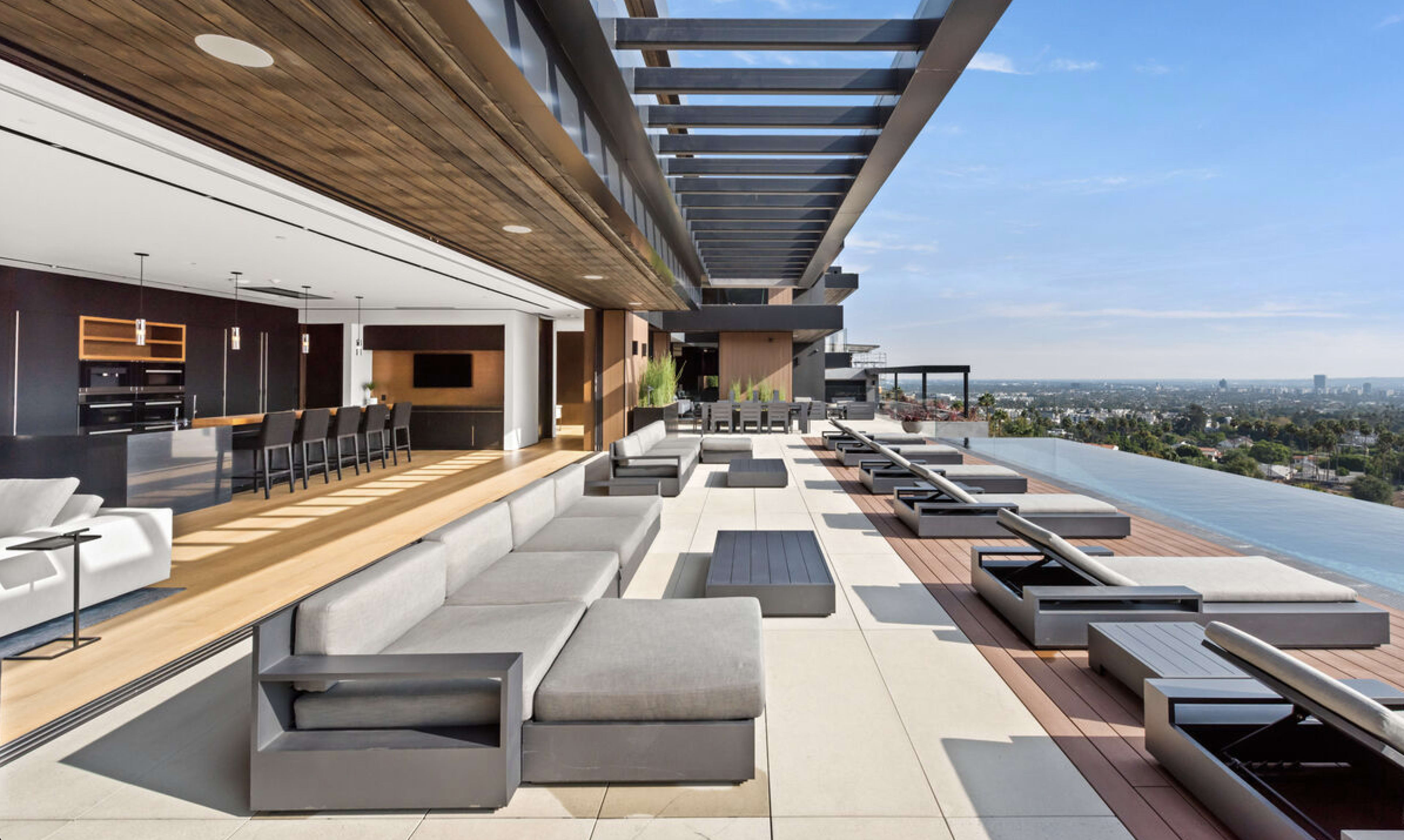 A modern outdoor terrace with lounge seating and an infinity pool, overlooking a city skyline.